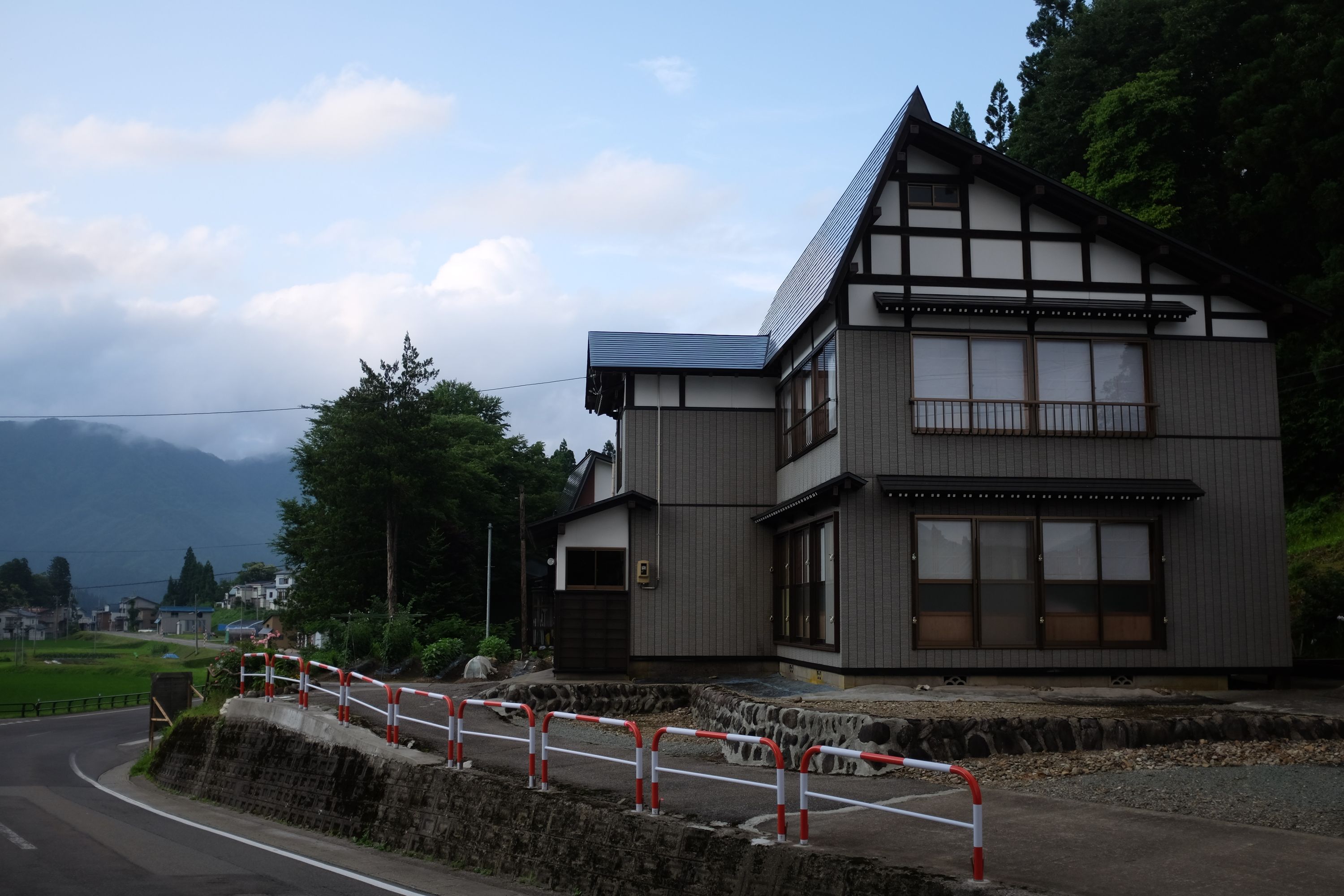 A large house with a steep, asymmetrically pitched roof by the side of the road.