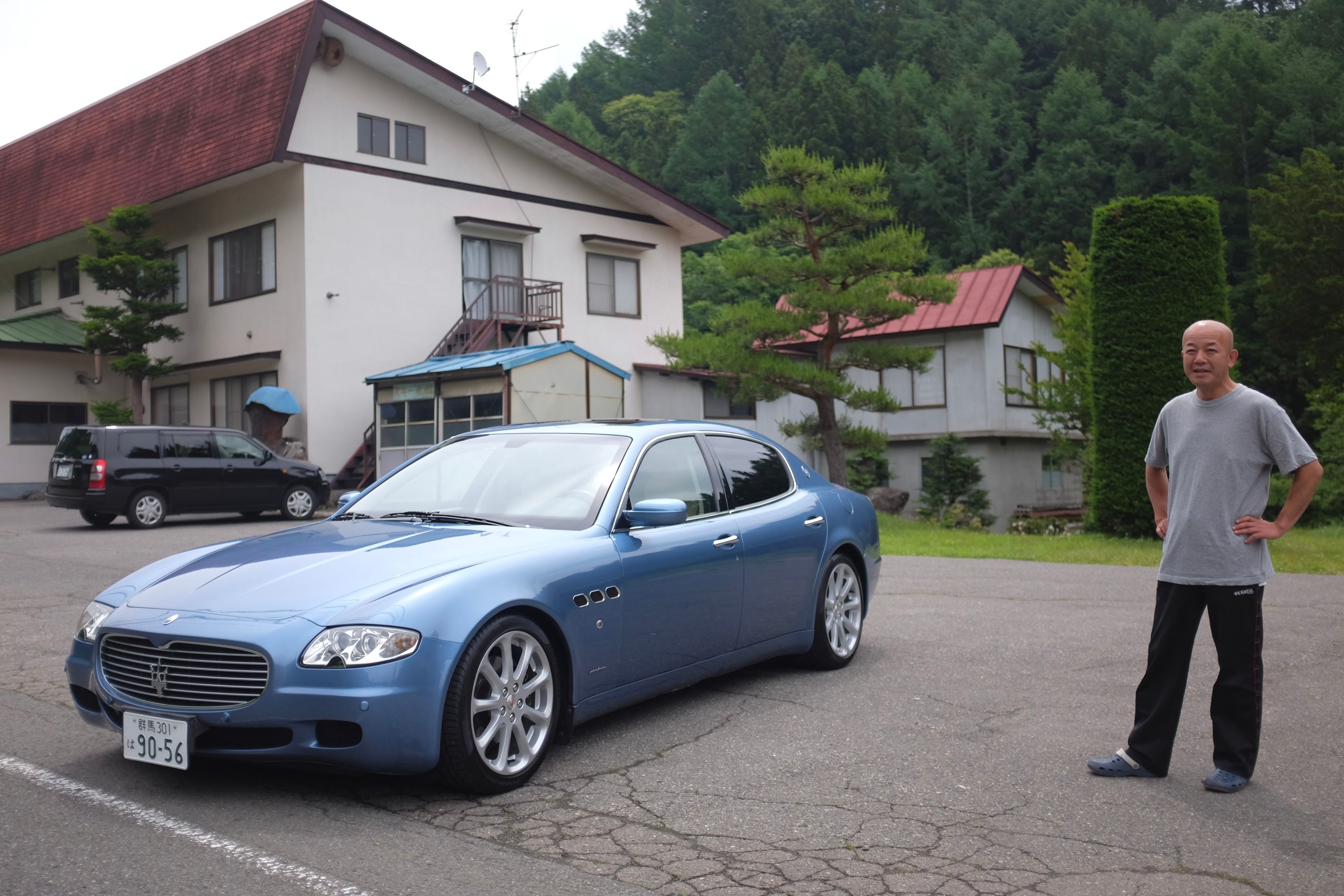 A man in grey t-shirt stand by his blue Maserati Quattroporte which broke down.