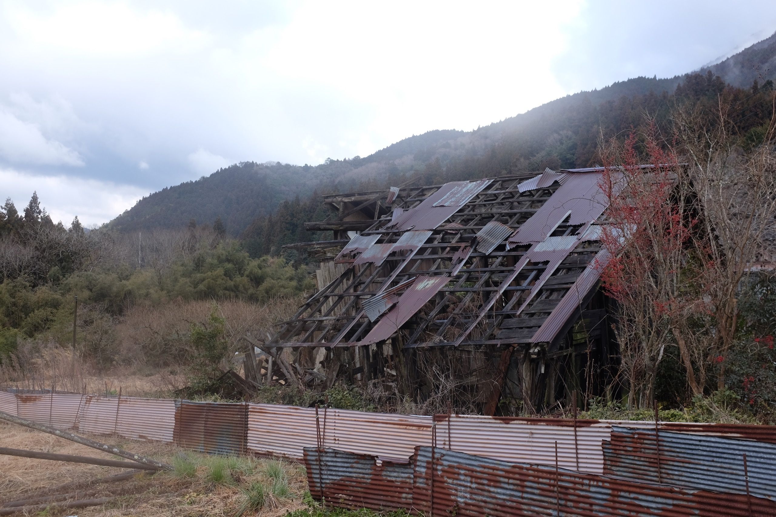 A large farmhouse in the last stage of decay by the side of the road.