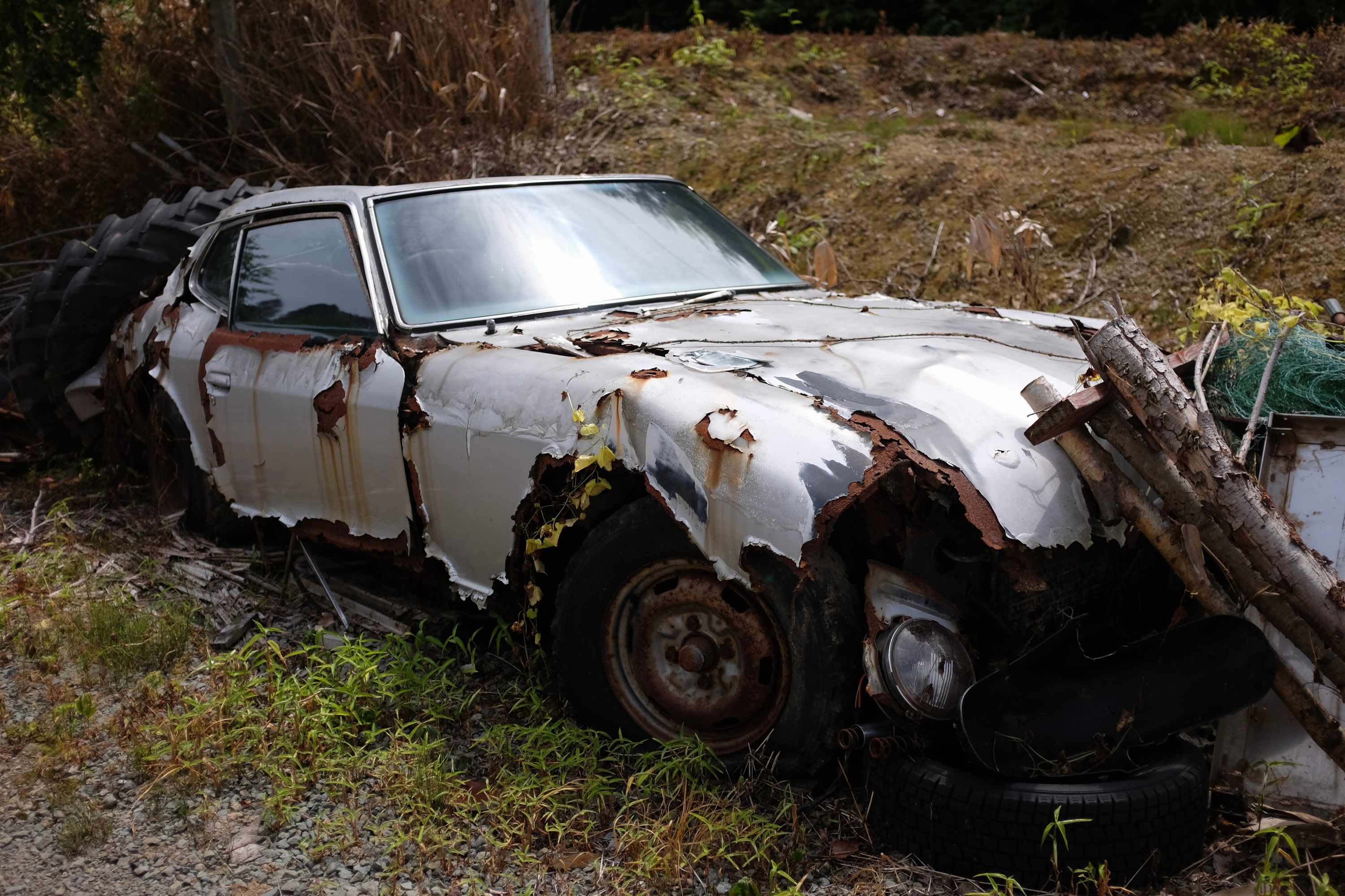 A white Datsun Z sports car in an advanced state of decomposition.