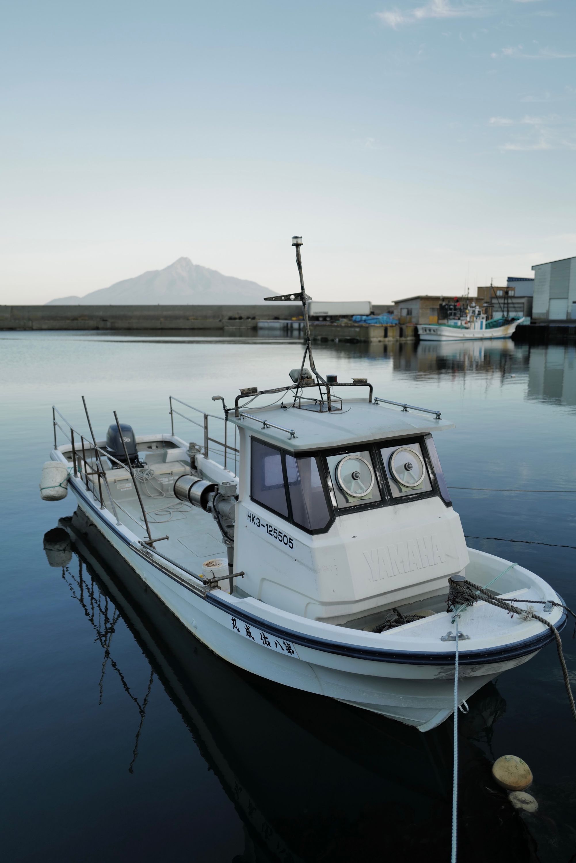 A small fishing boat in a harbor, with Mount Rishiri on the horizon behind it