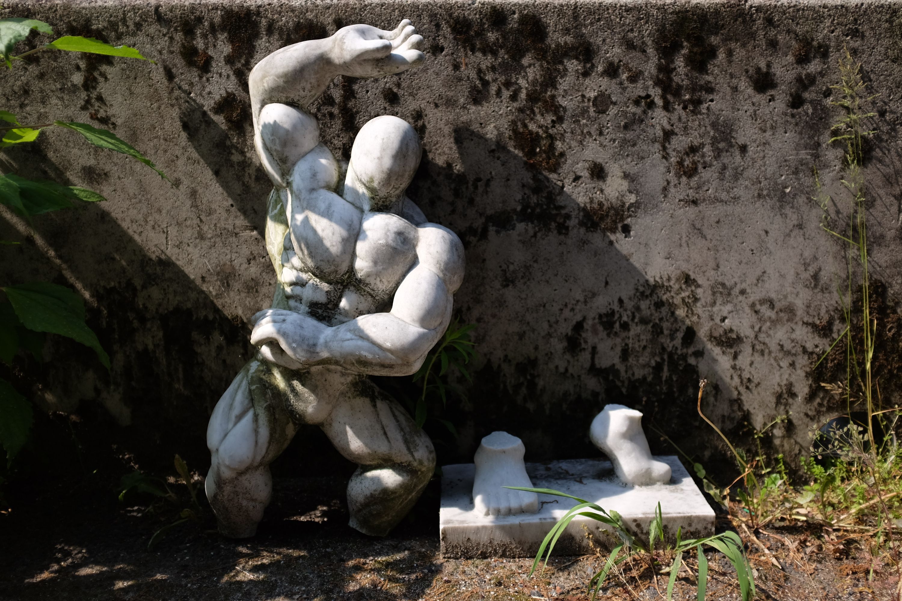 Statue of a very muscular man with his feet on a separate pedestal.