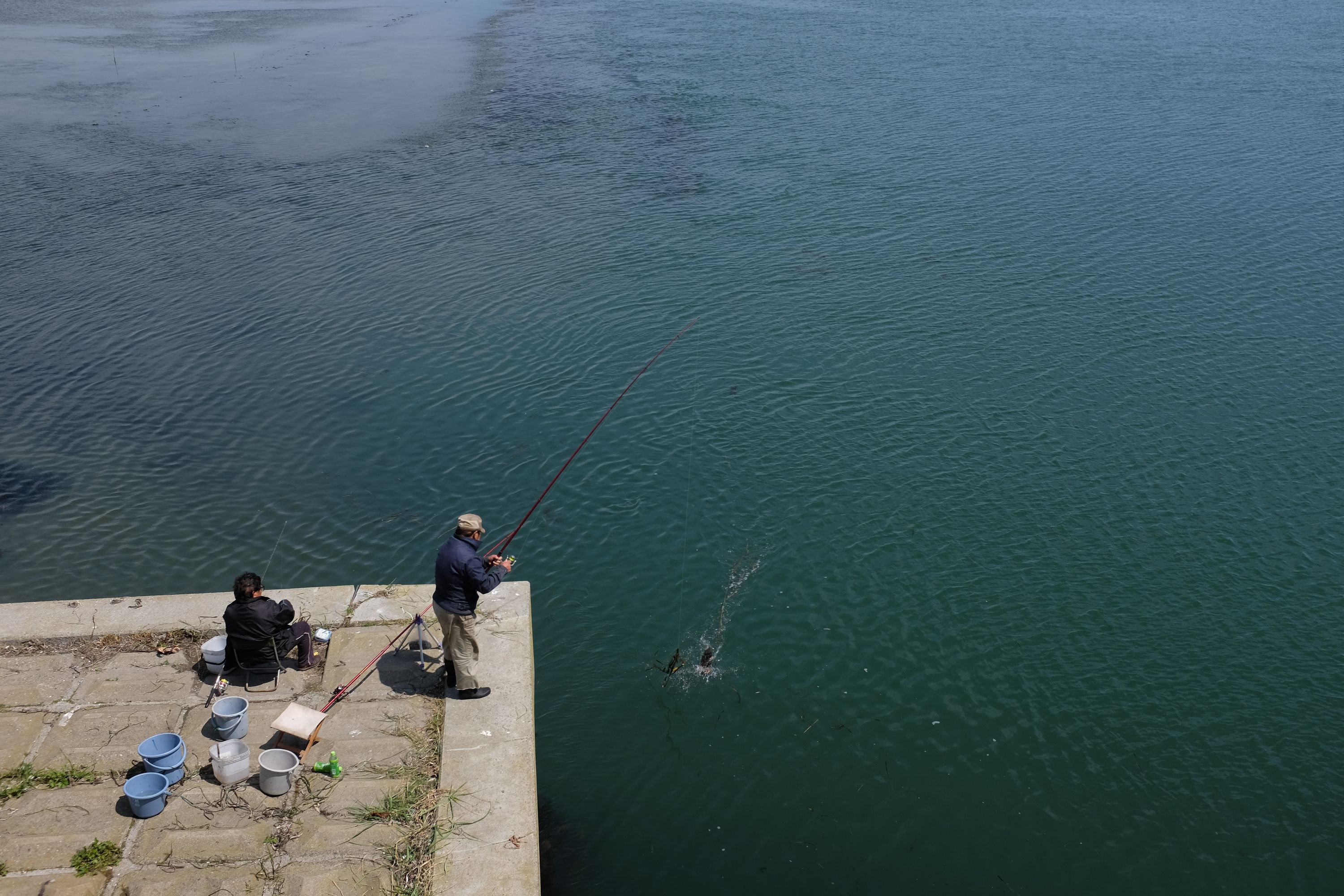 Two men fish from a pier.