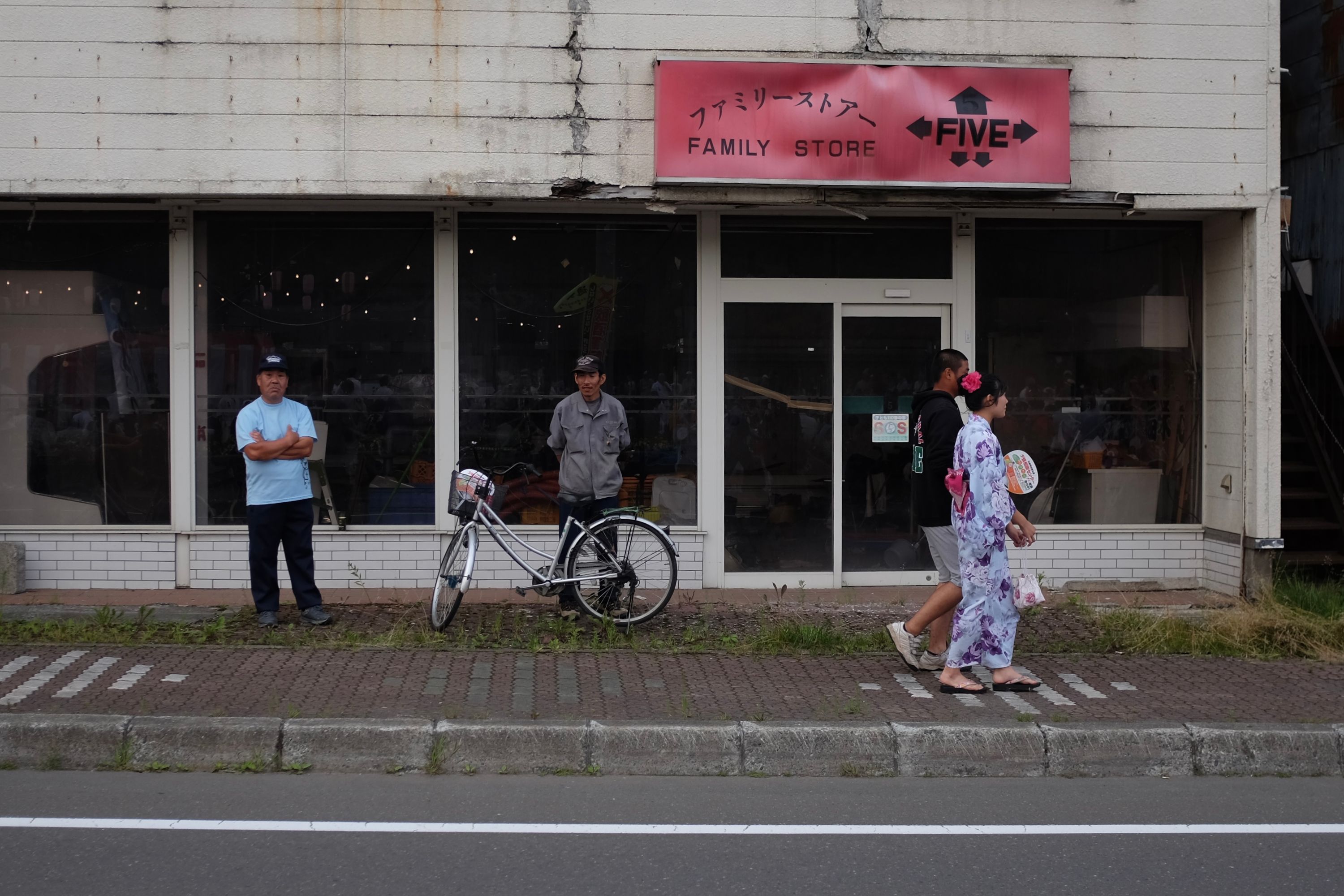 A couple in festival clothes walks by a shop, with two older men standing by.