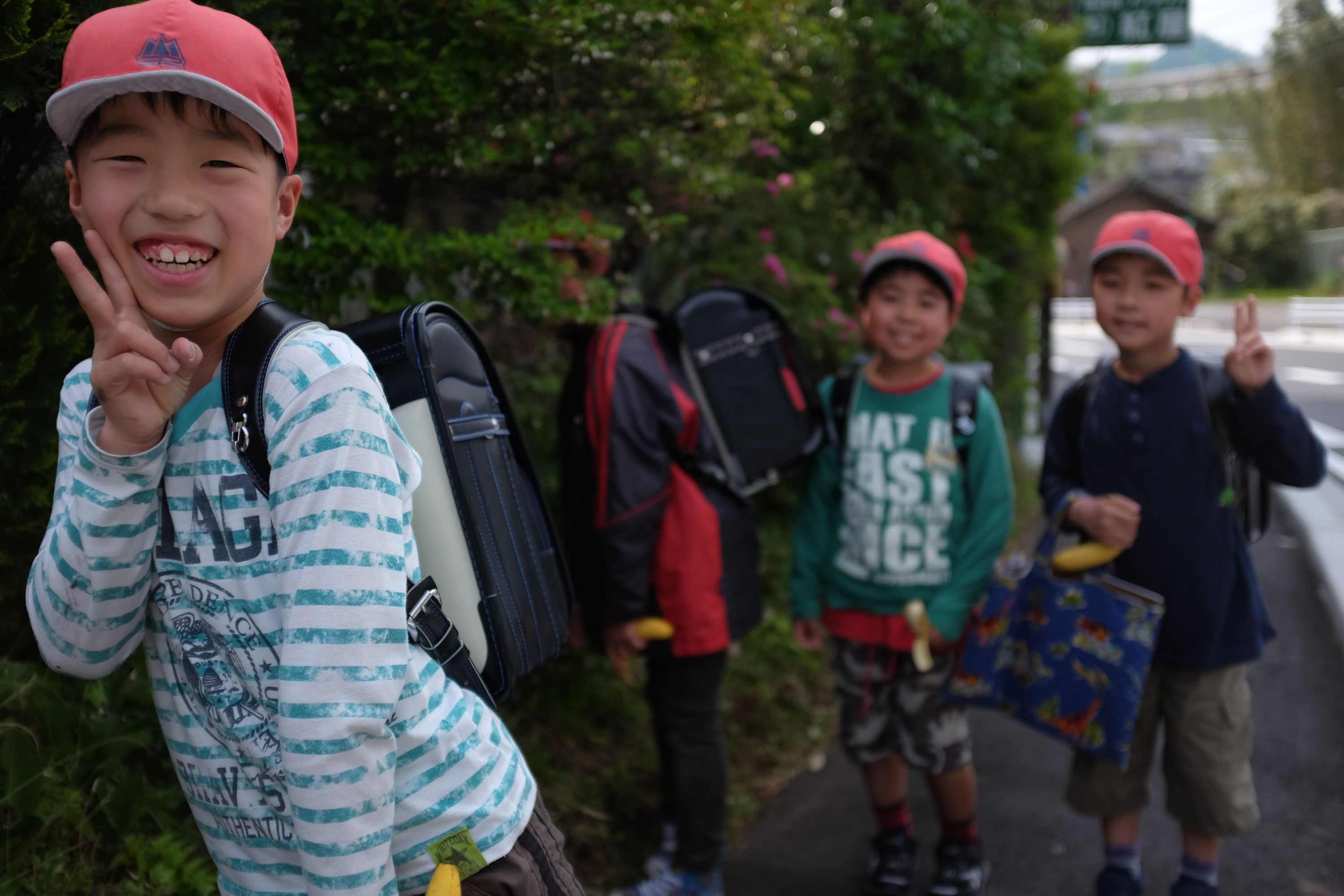 A group of schoolchildren in red baseball caps make V-signs for the camera.