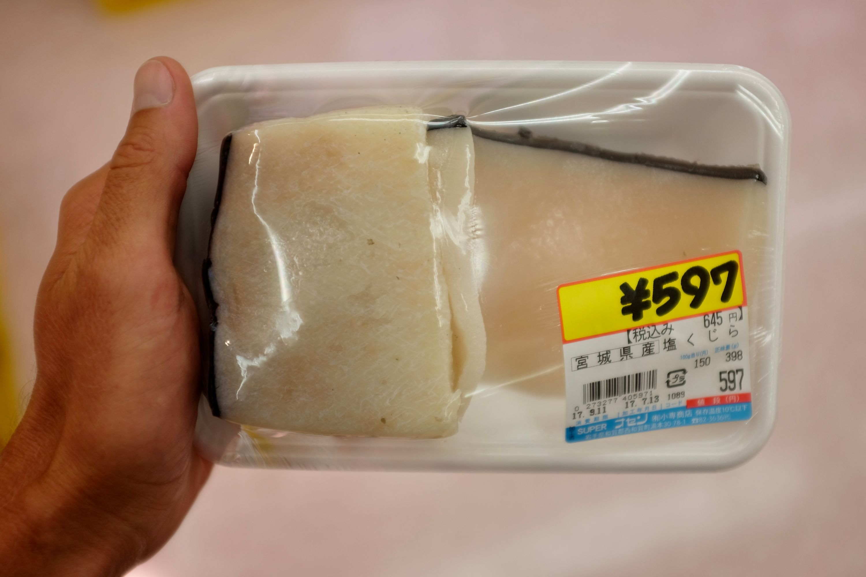 The author holds a piece of packaged whale meat costing ¥597 in his left hand.