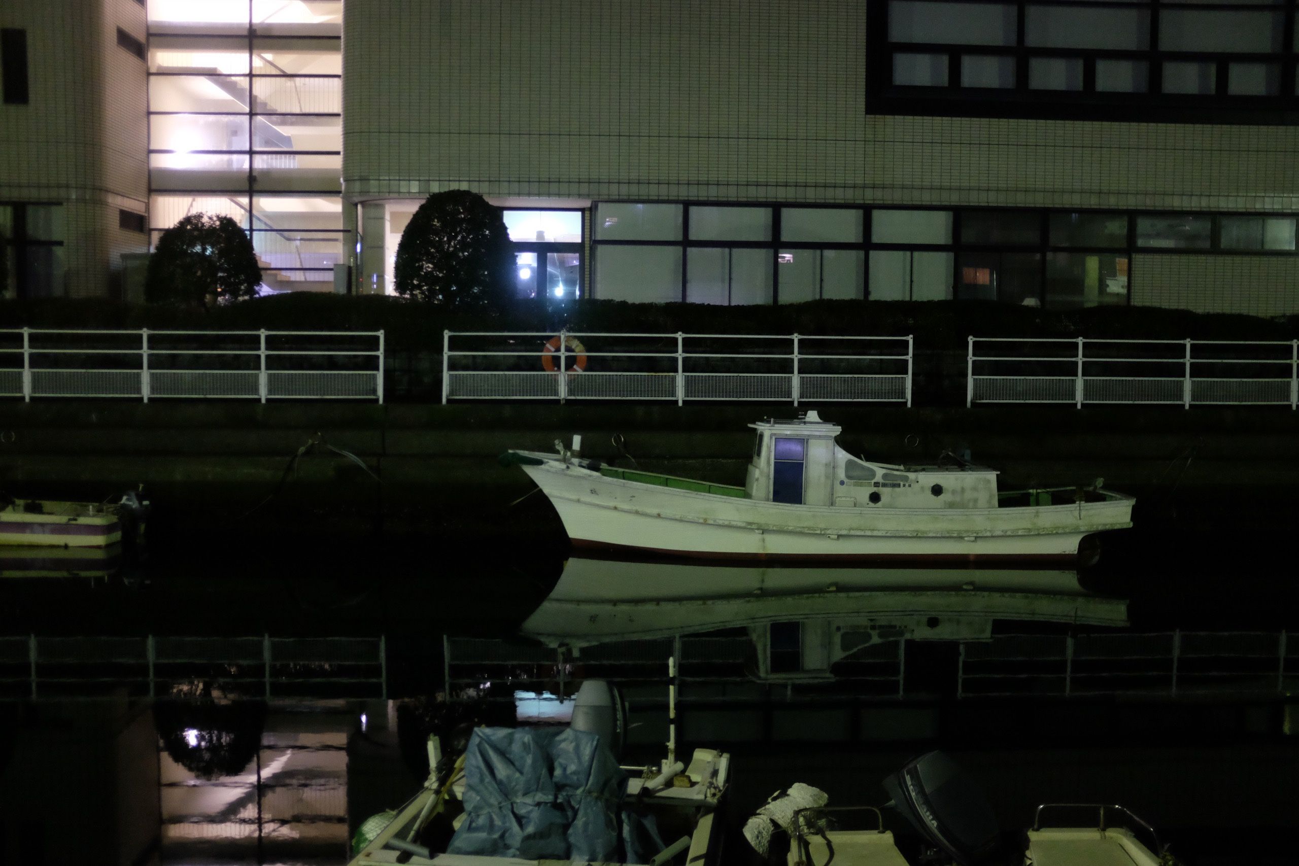 A small boat is parked in a canal that runs between office buildings.