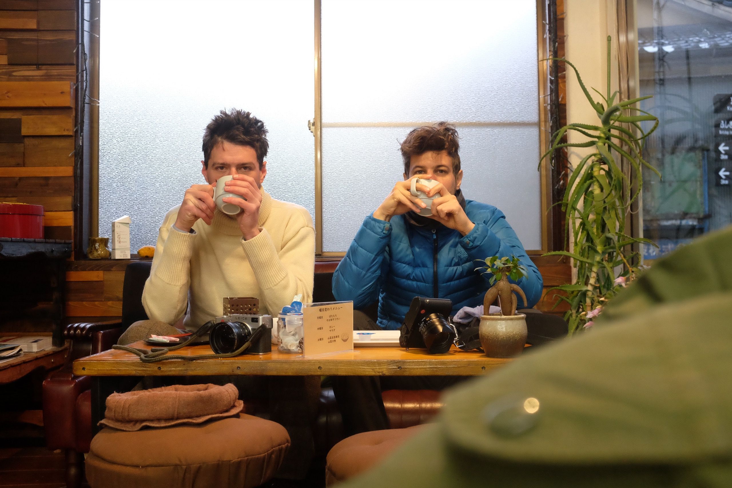 Two men, the author and Gyula Simonyi, drink coffees at a table, dressed in winter clothes, looking cold and tired.