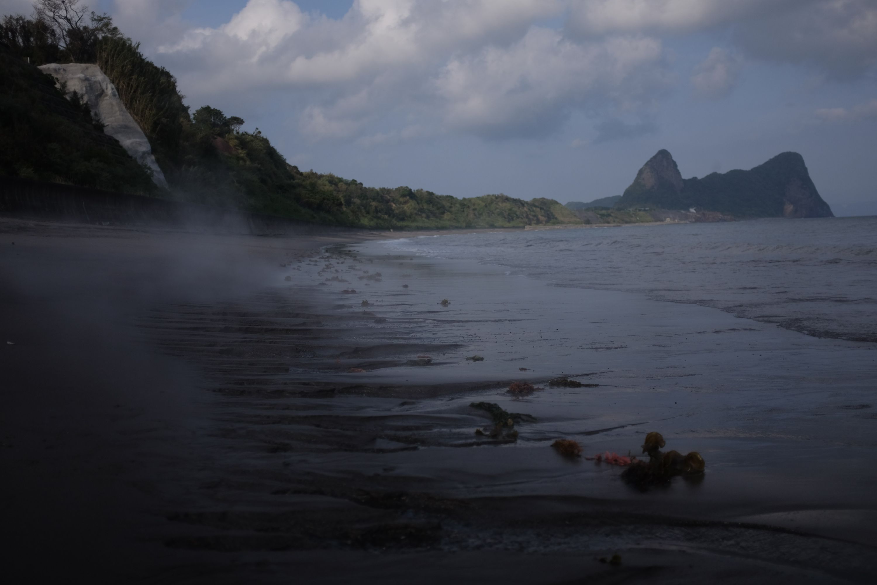 Steam rises from the sand on a seashore.