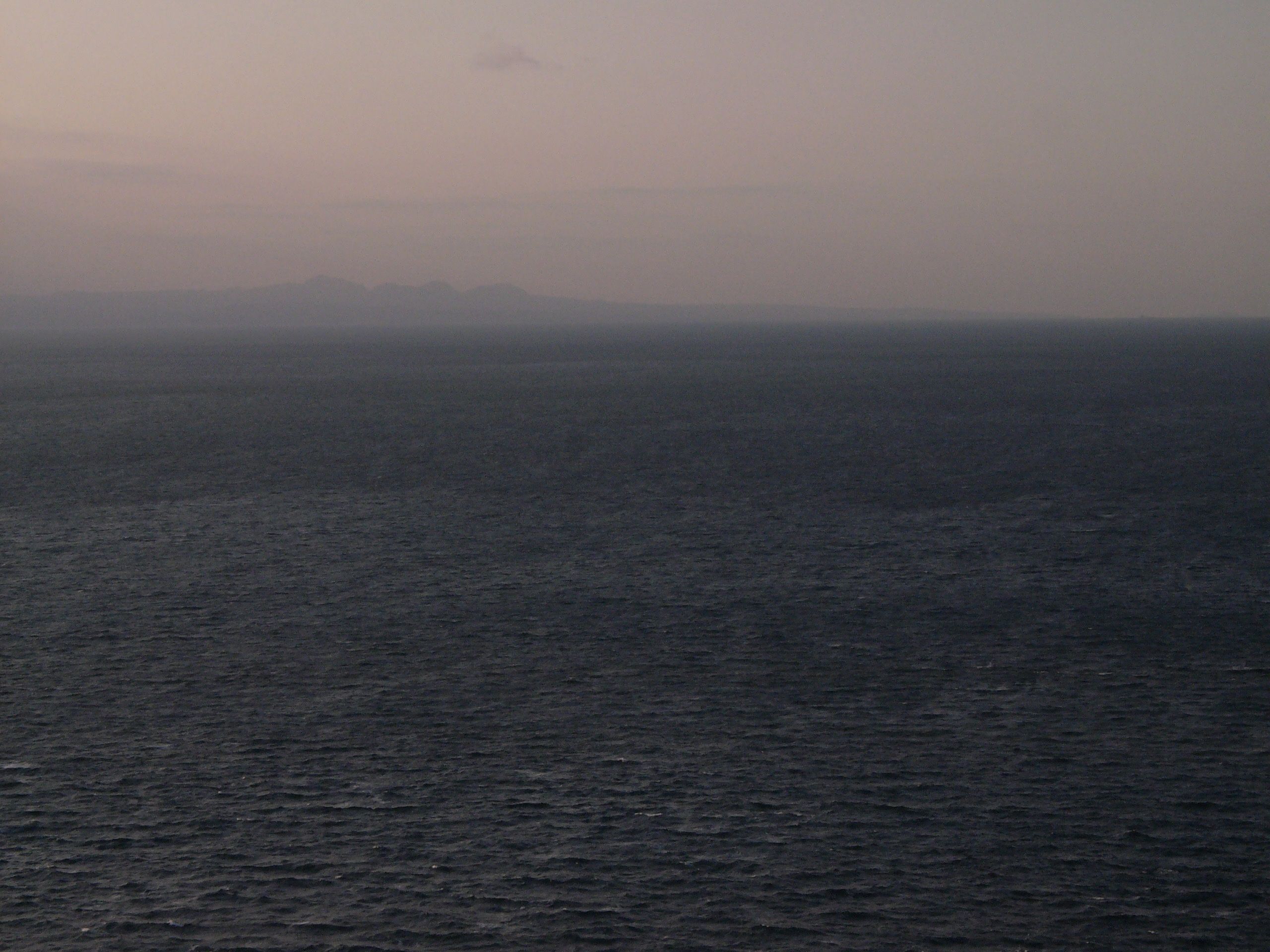 The silhouette of a low, craggy mountain across the sea at dusk.