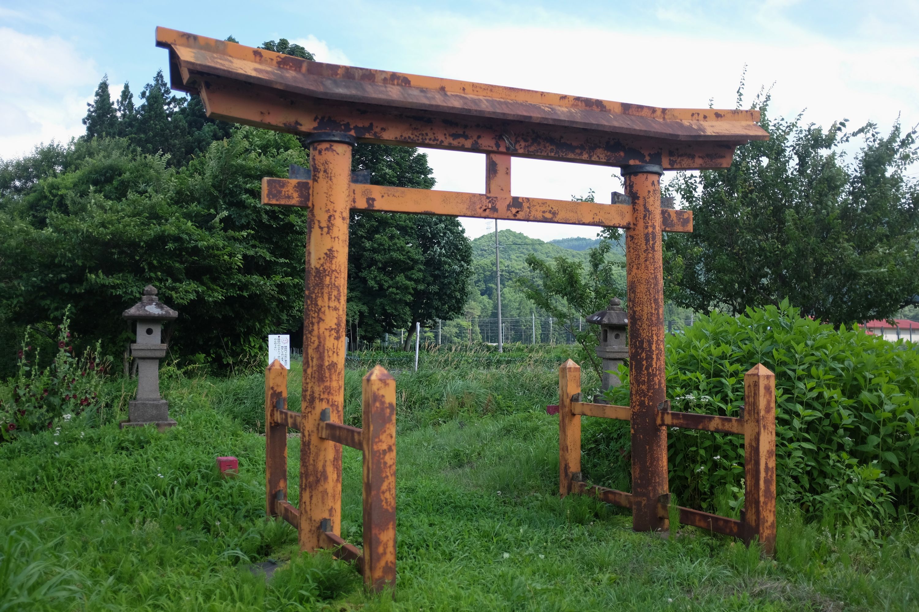 An unusual shrine gate made of metal, painted yellow and rusting.