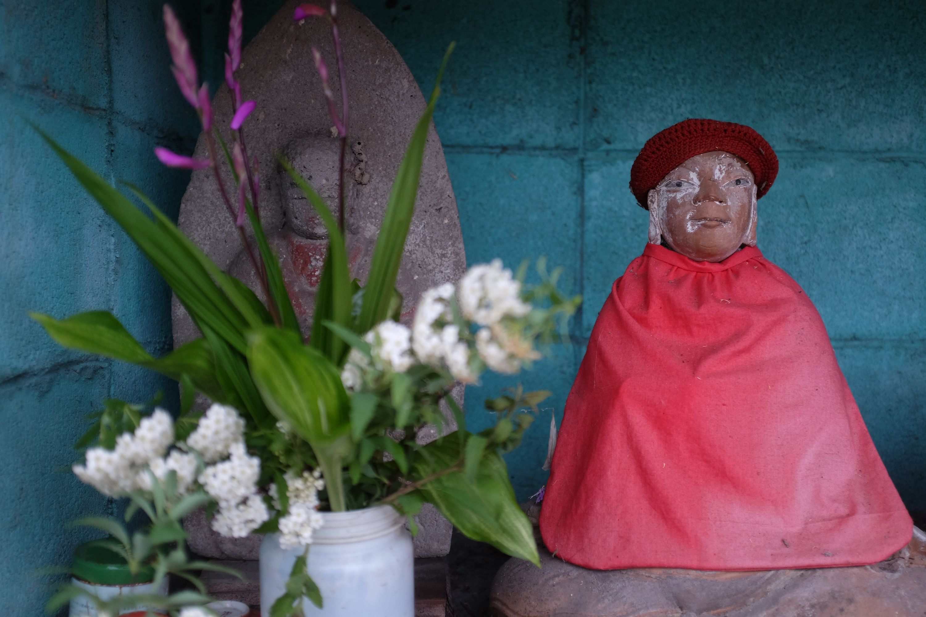 Two Buddhist statues, one dressed in red, on a small altar, with a vase of flowers.