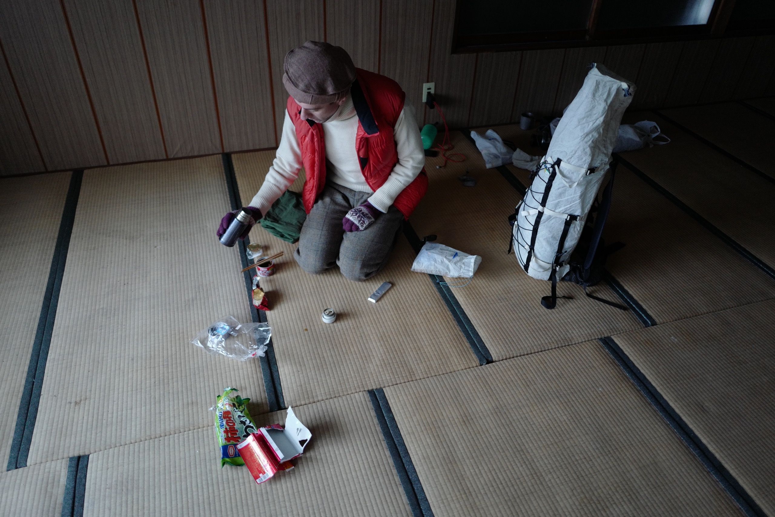 A man in winter clothes, the author, kneels on a tatami floor and pours coffee from a thermos.