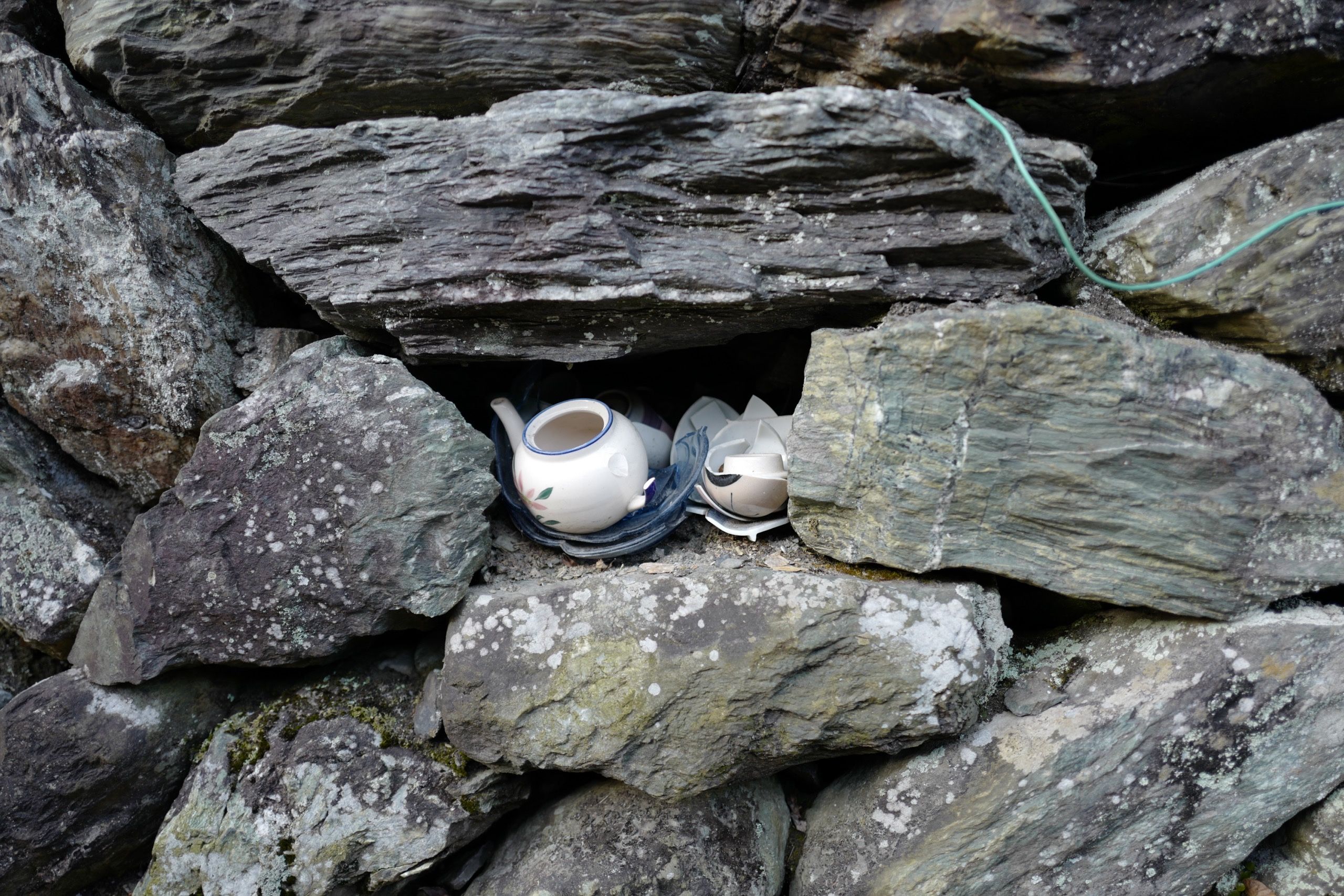 Closeup of a stone wall with pieces of broken pottery between its stones.