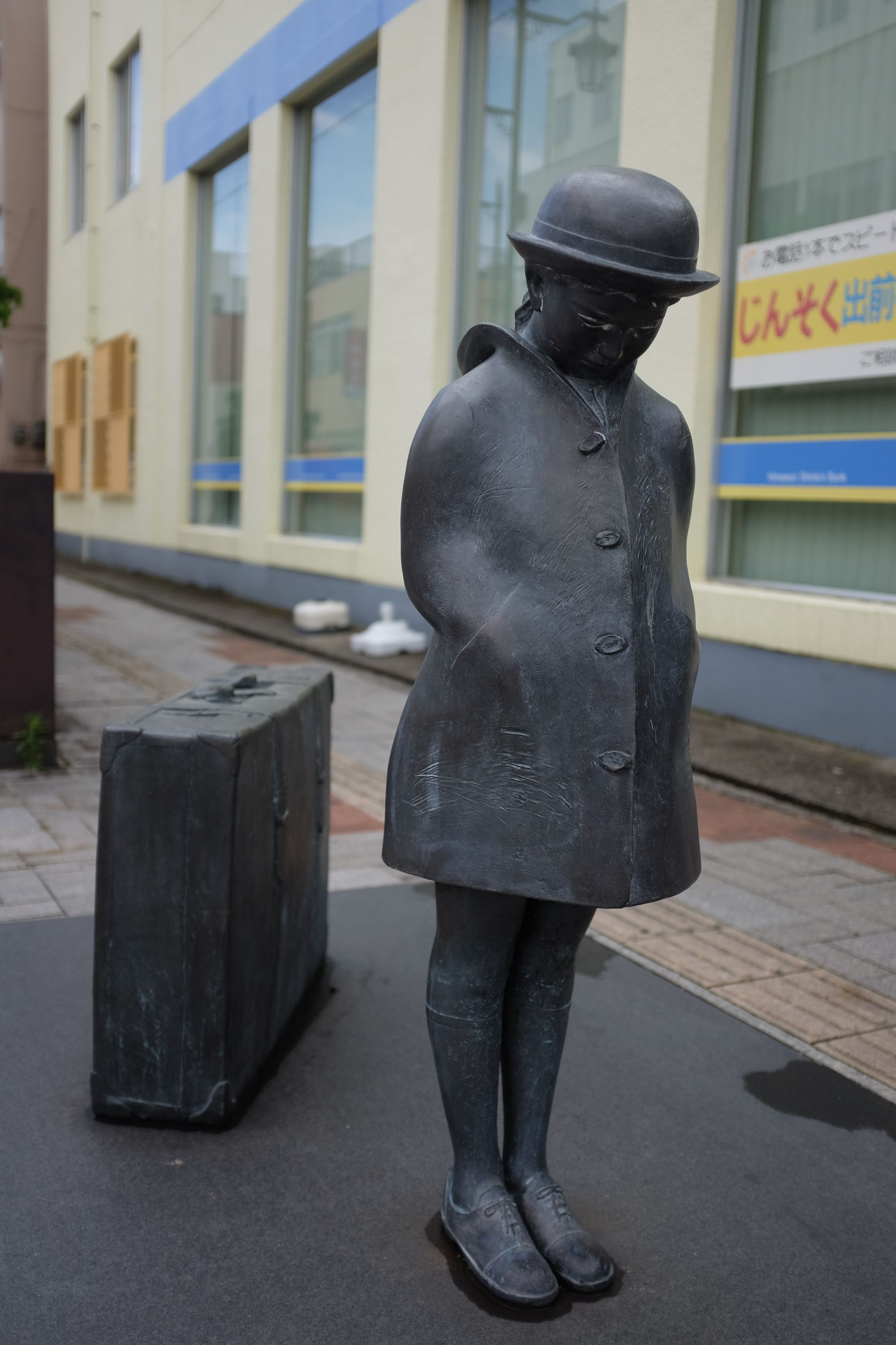 Bronze statue of a girl about to depart for a journey and looking melancholy.