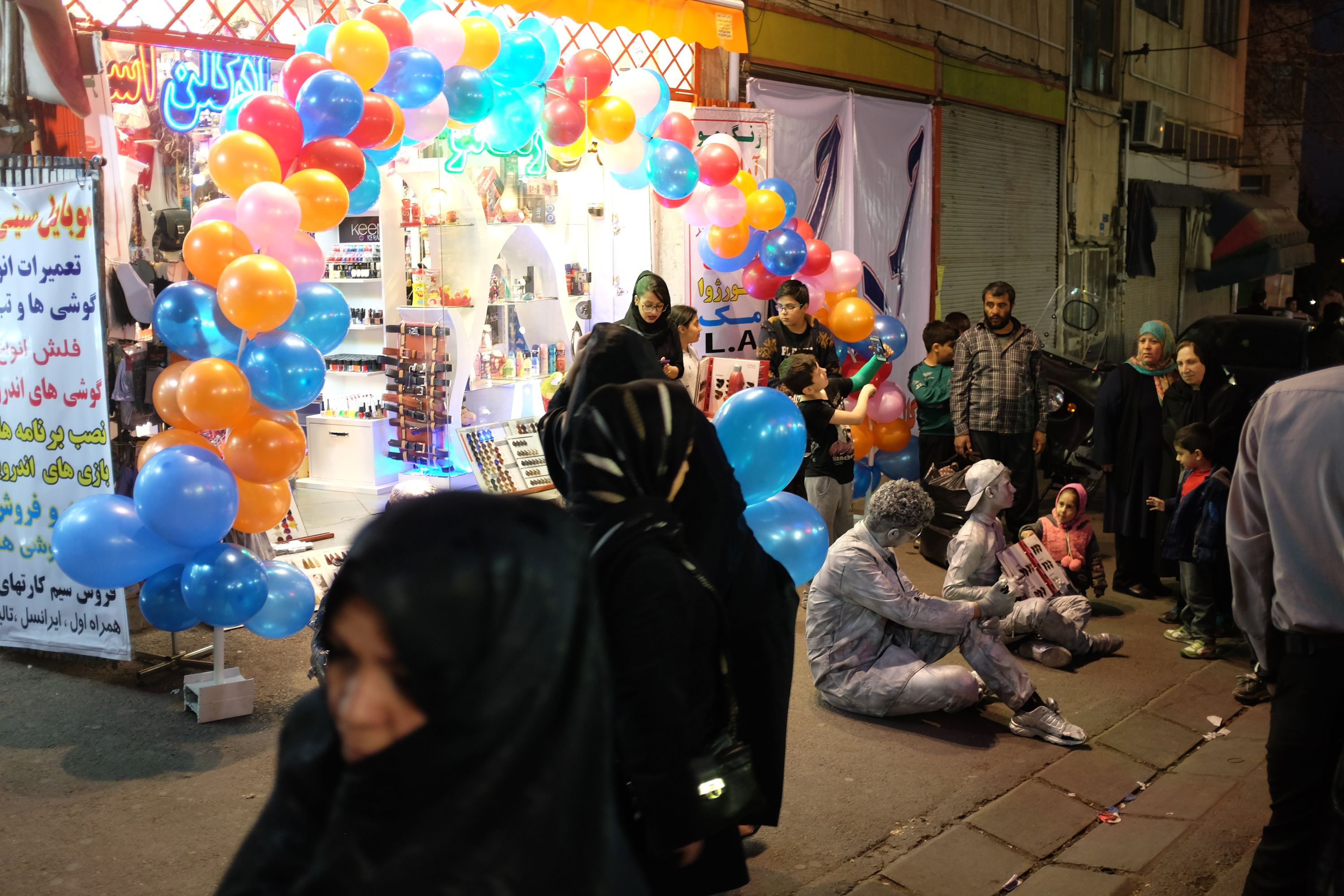 Women walk past a shop with musicians playing in front of it.