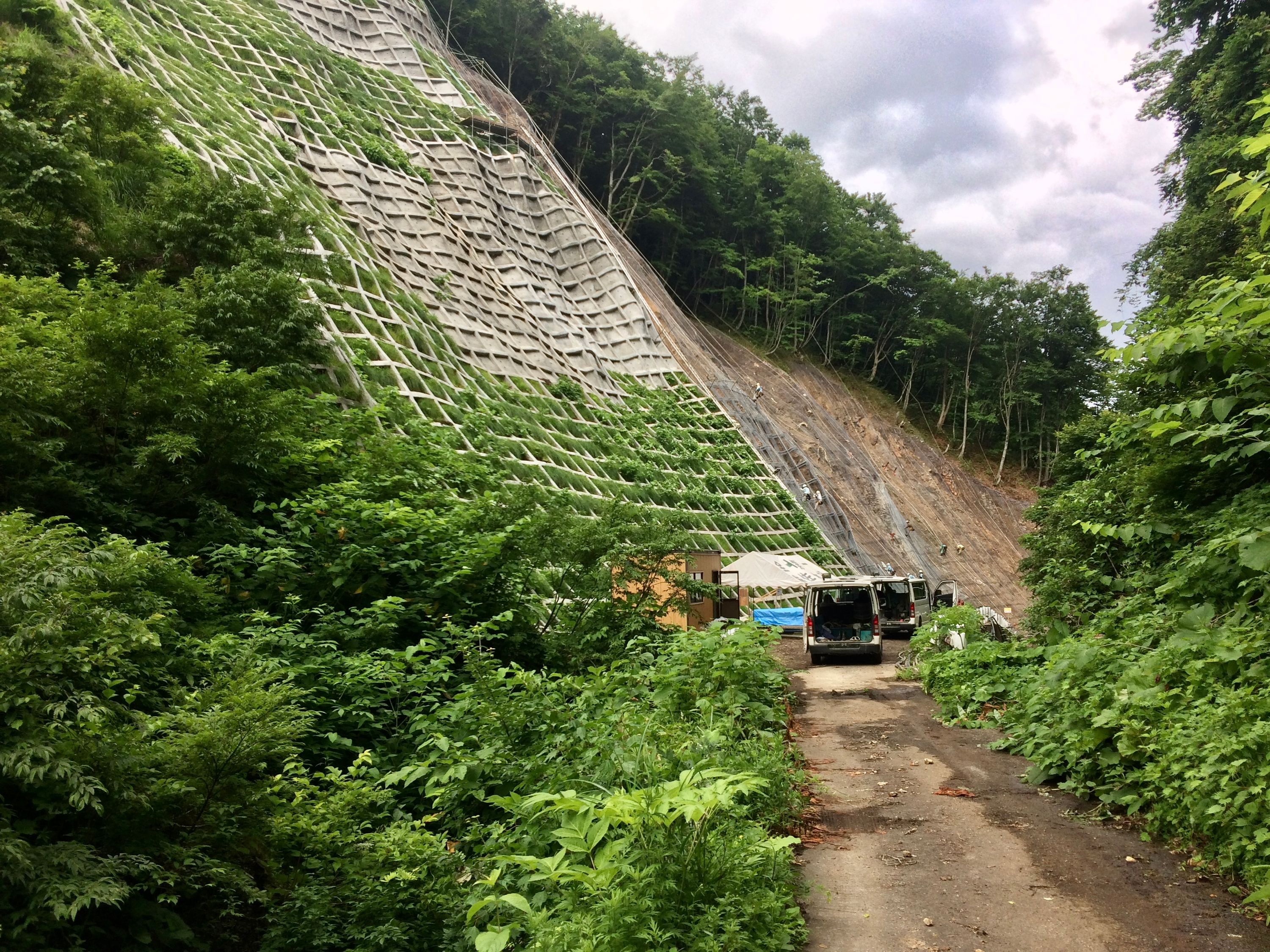 A concrete retaining wall being constructed above a dirt road.