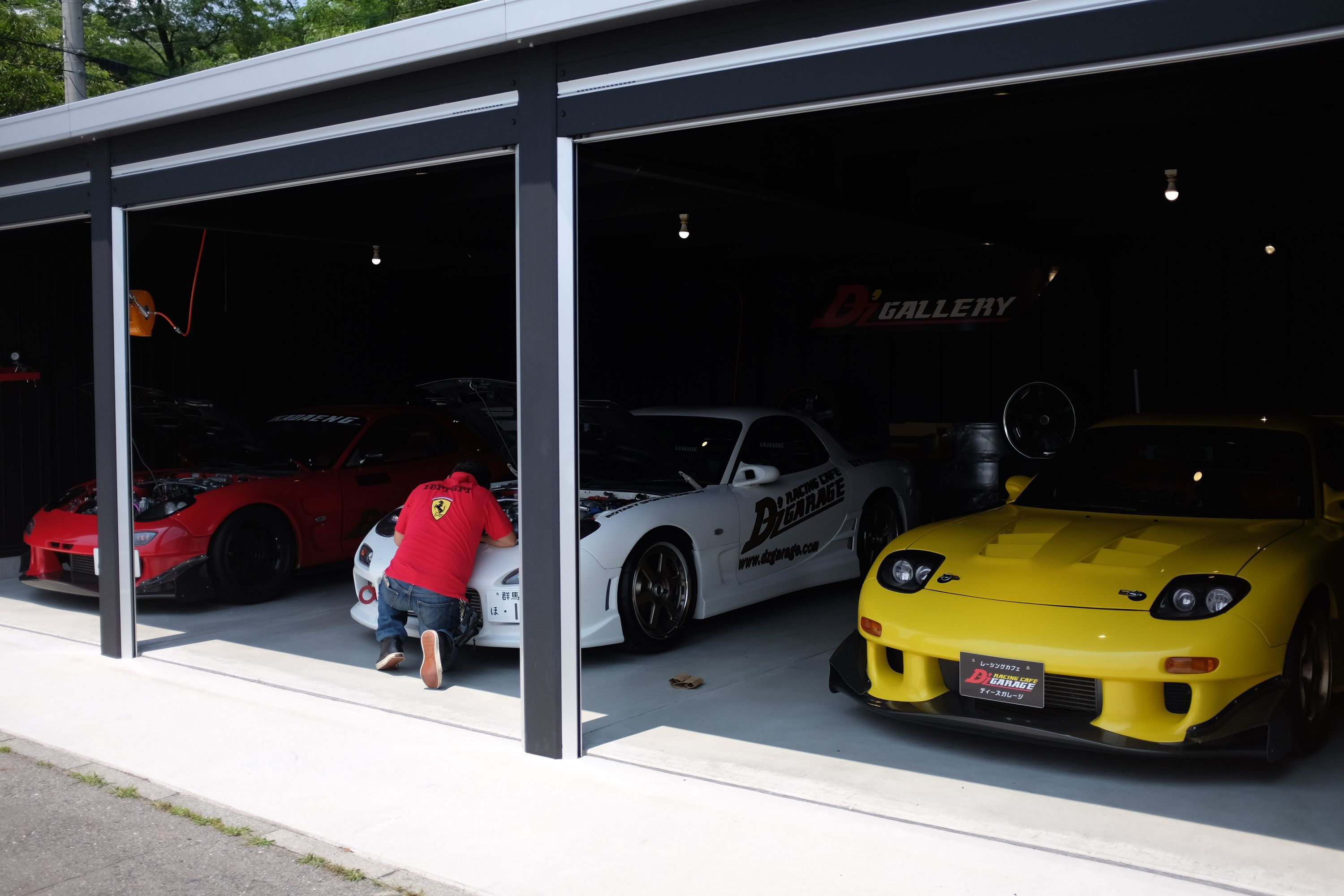 A mechanic works on three colorful racing cars in a garage.