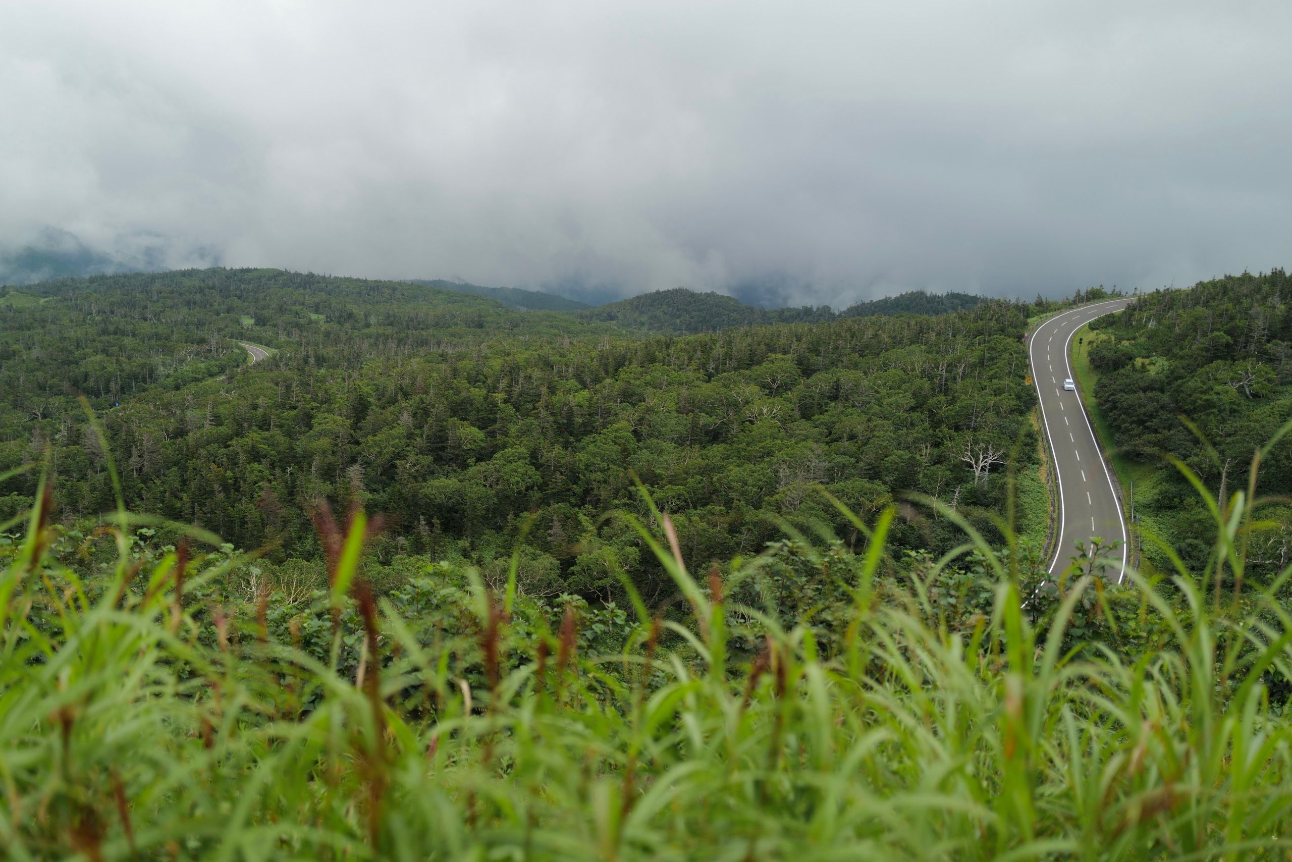 A mountain road in the distance cuts through a verdant green landscape.