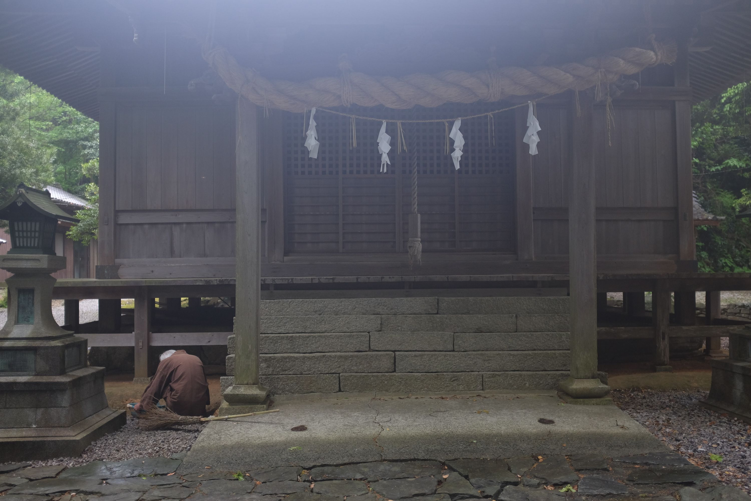 A groundskeeper, dressed in earth tones, squats before his shrine.