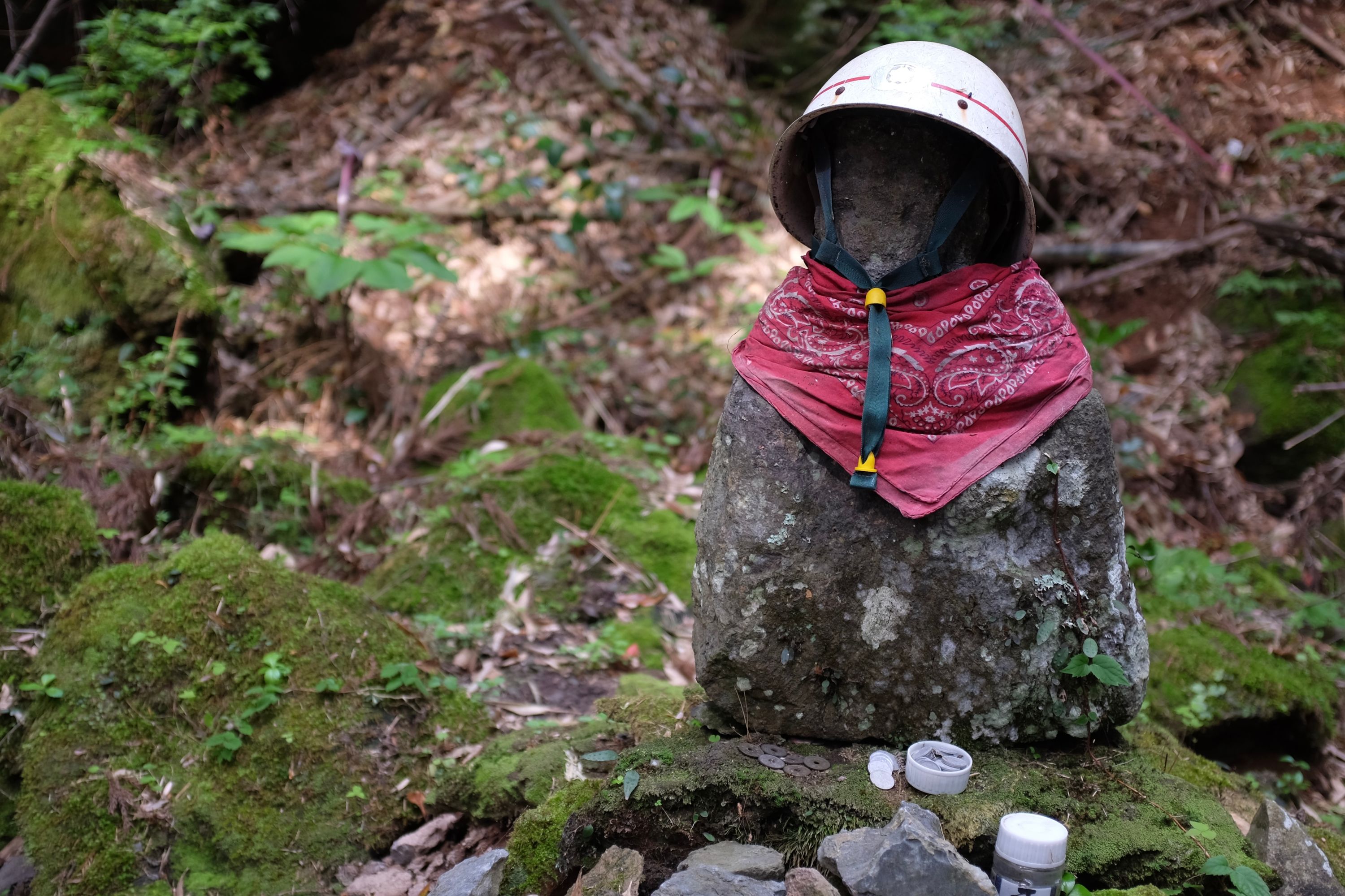 A Buddhist roadside statue wears a red bandanna and a white hard hat.