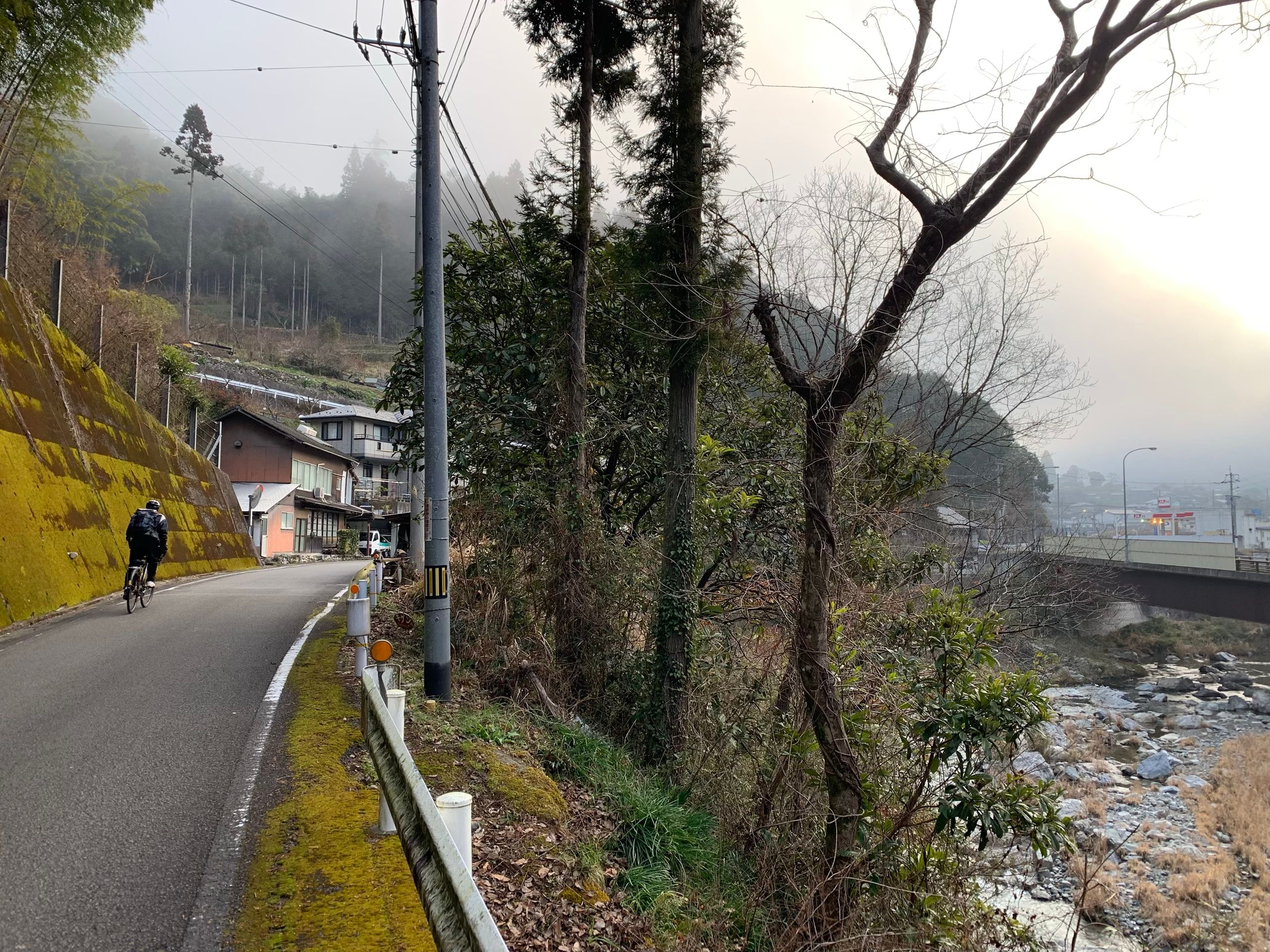 A man on a fast bike pedals into a village by a stream.