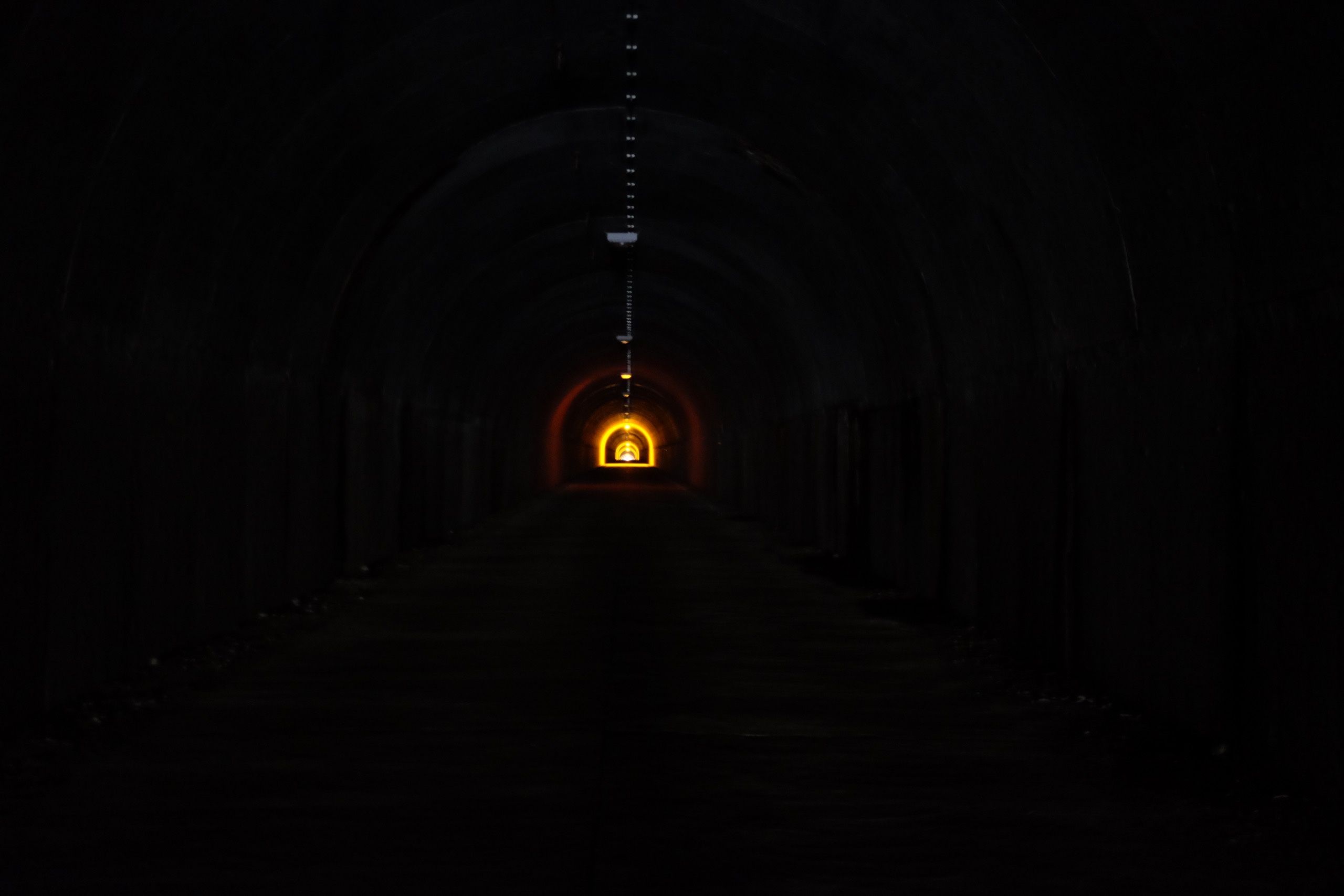 Looking along a pitch-black tunnel with some artificial lights in the distance.