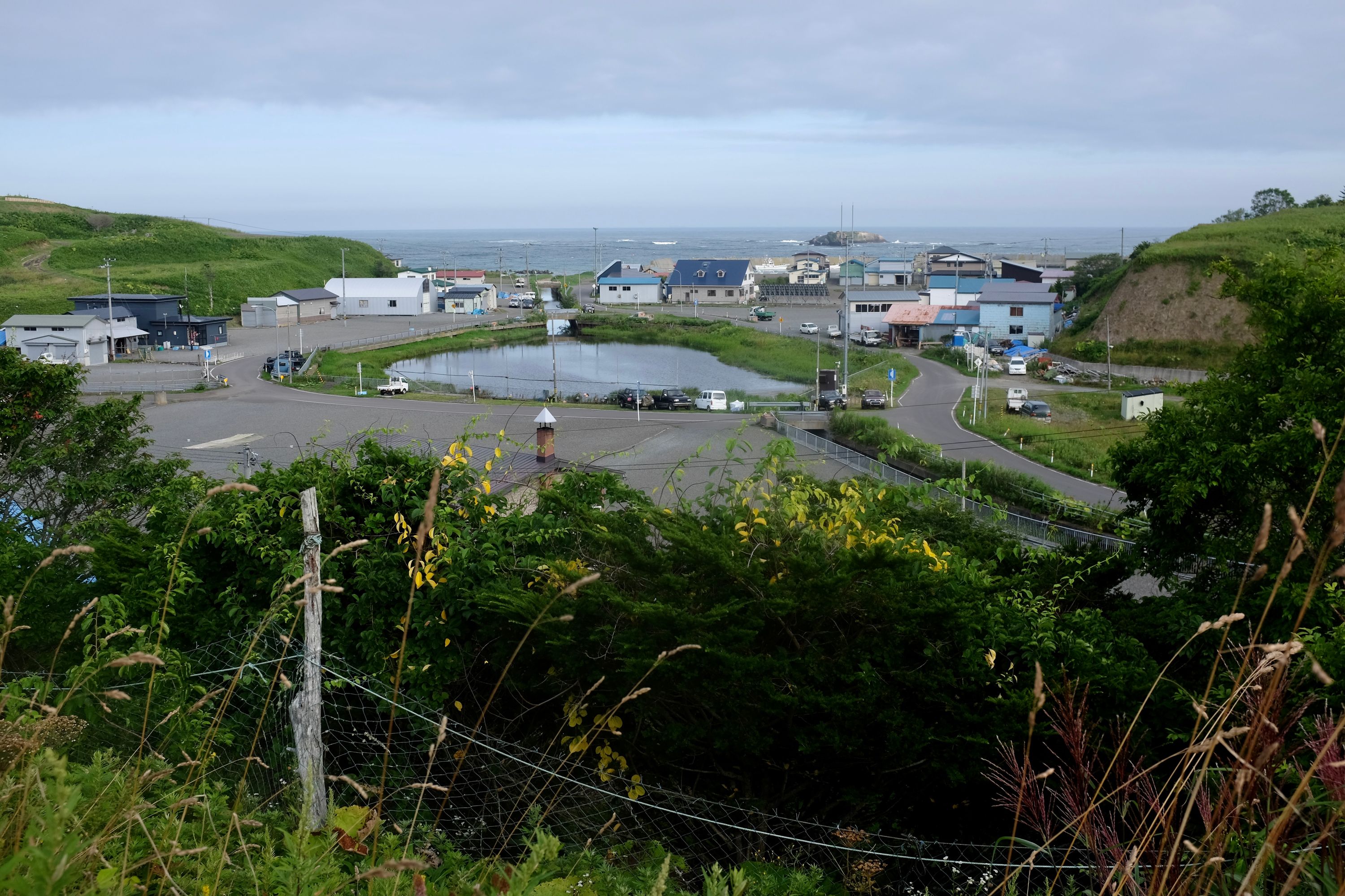 A small fishing village nestled between two green hills, the ocean beyond it.