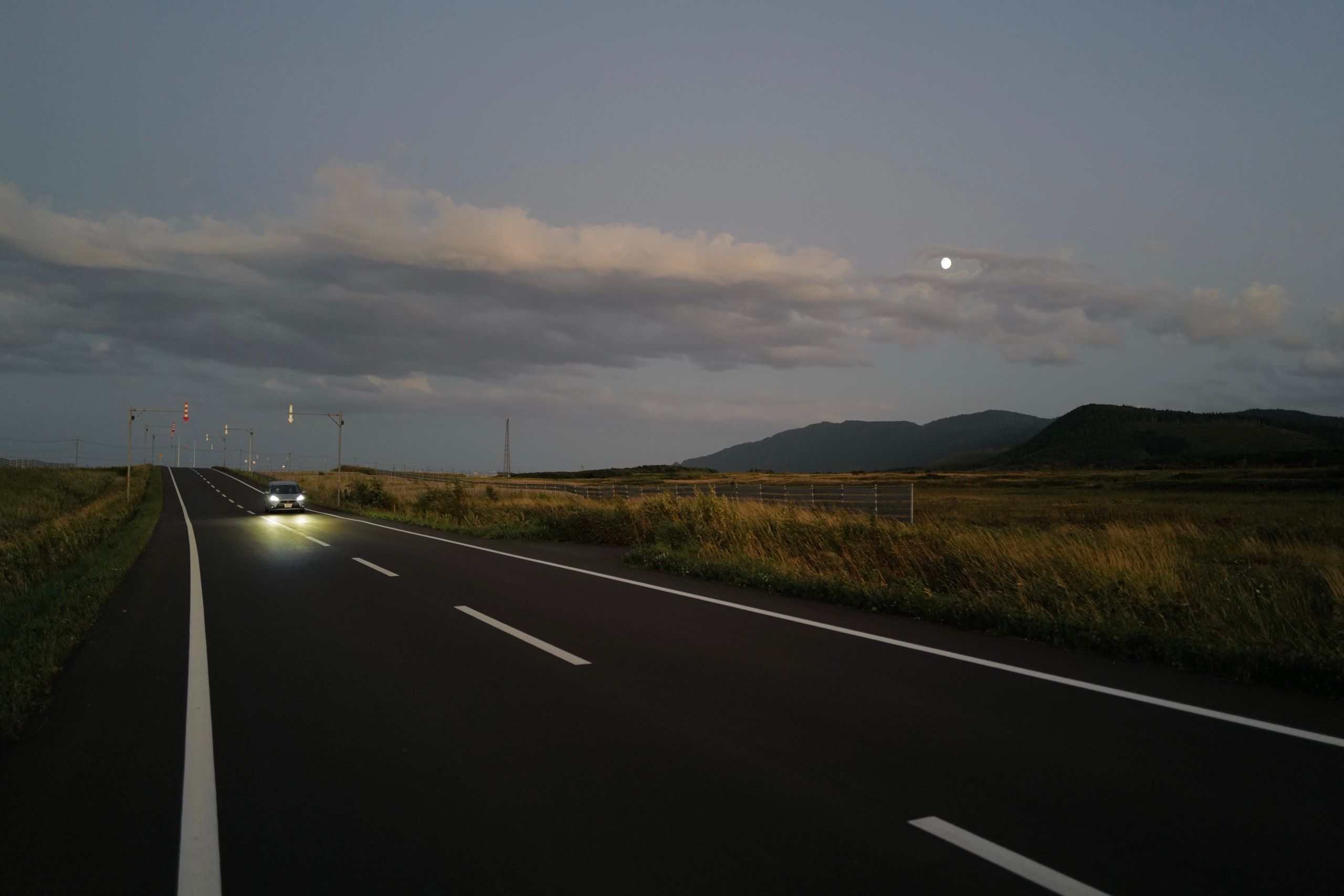 A car drives down a country road in the moonlight