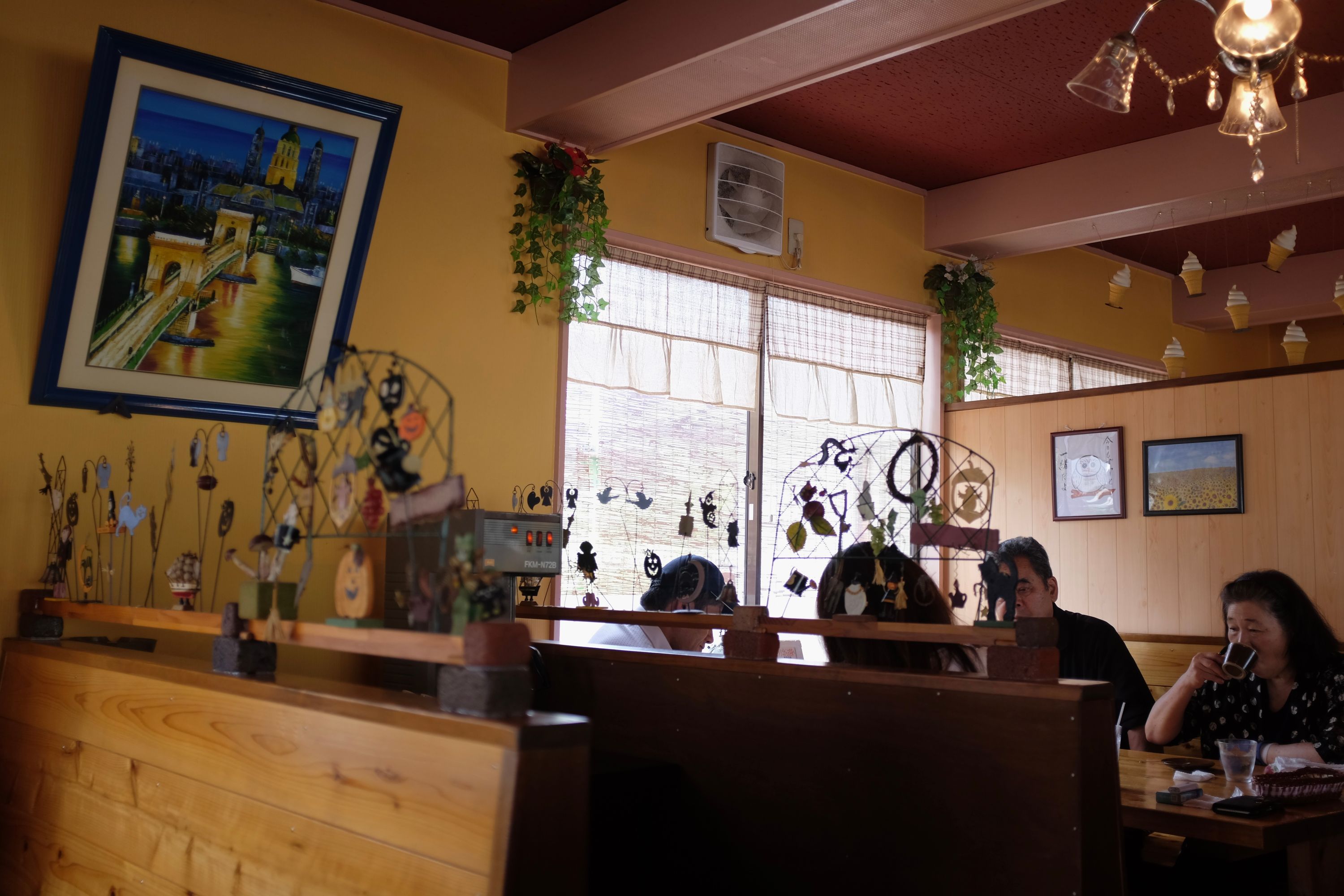 A family eats dinner in a countryside restaurant, next to a picture showing the center of Budapest painted from memory.