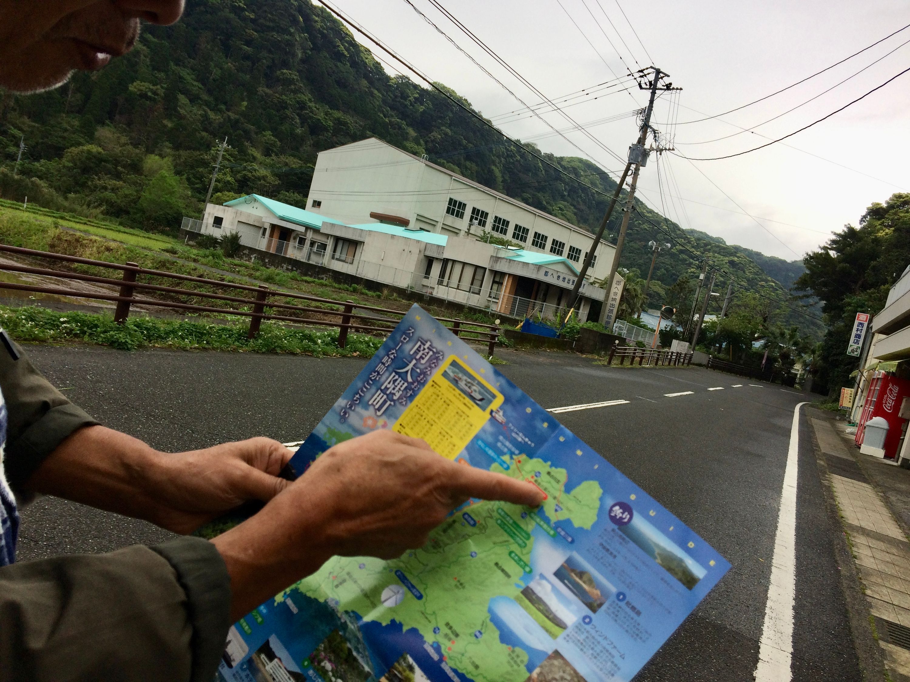 A man points at a tourist map of Minamiōsumi Town, whose outline looks like a jumping dog.