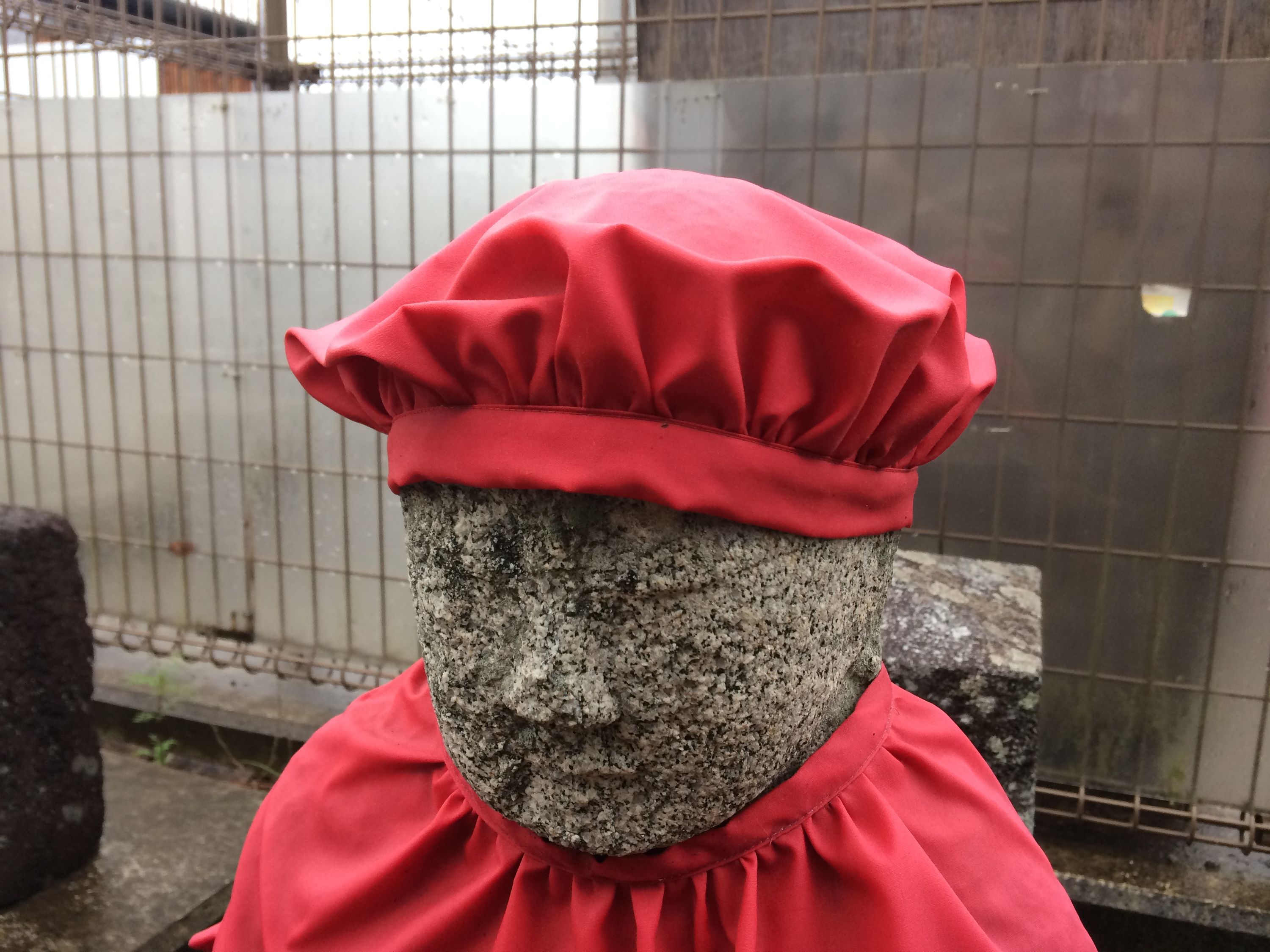 The head of a buddhist roadside deity dressed in a red cap and a red apron.