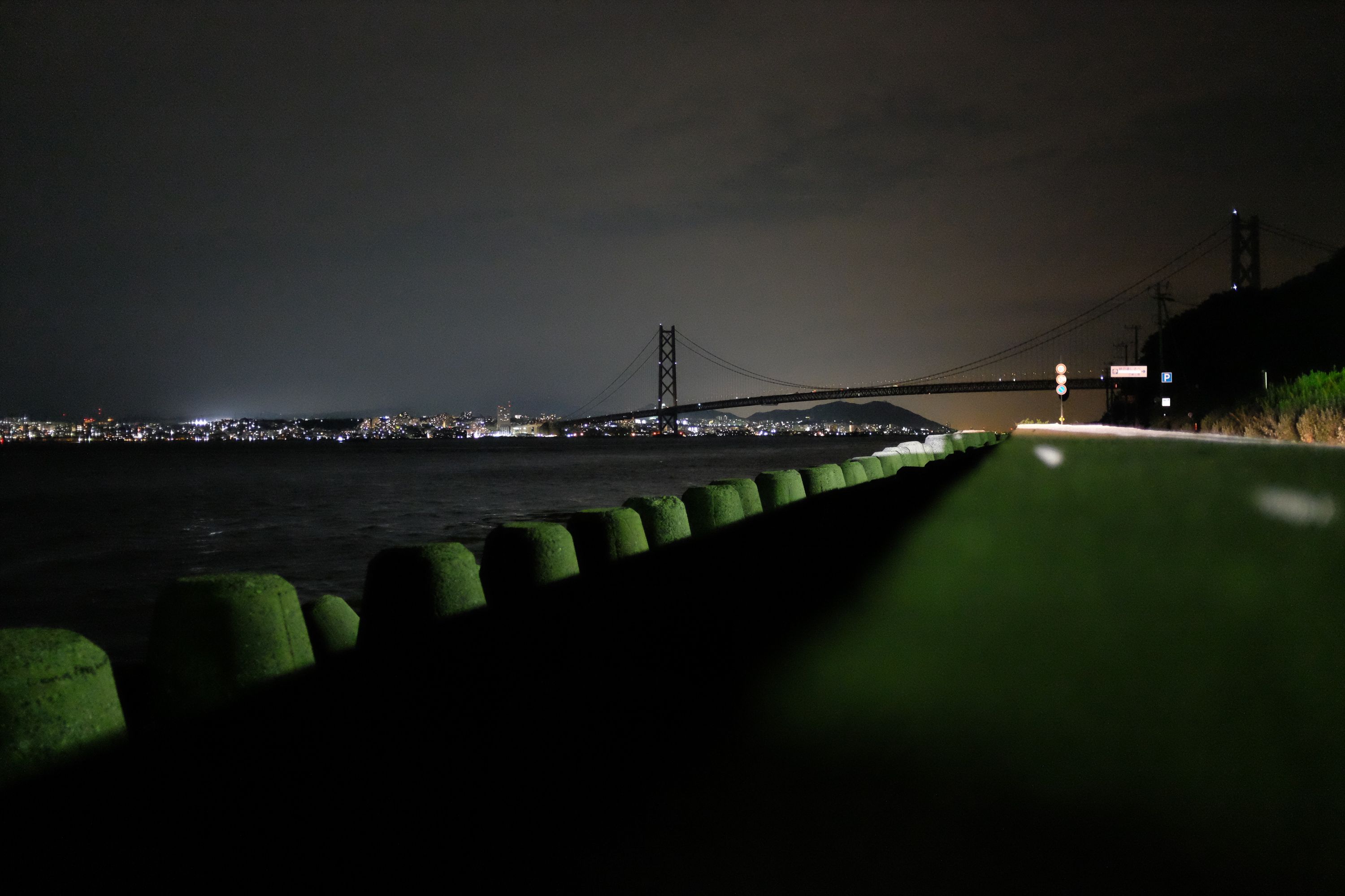 The world‘s longest suspension bridge, the Akashi Kaikyō, against a cloudy night sky lit by the lights of a city, Kōbe.
