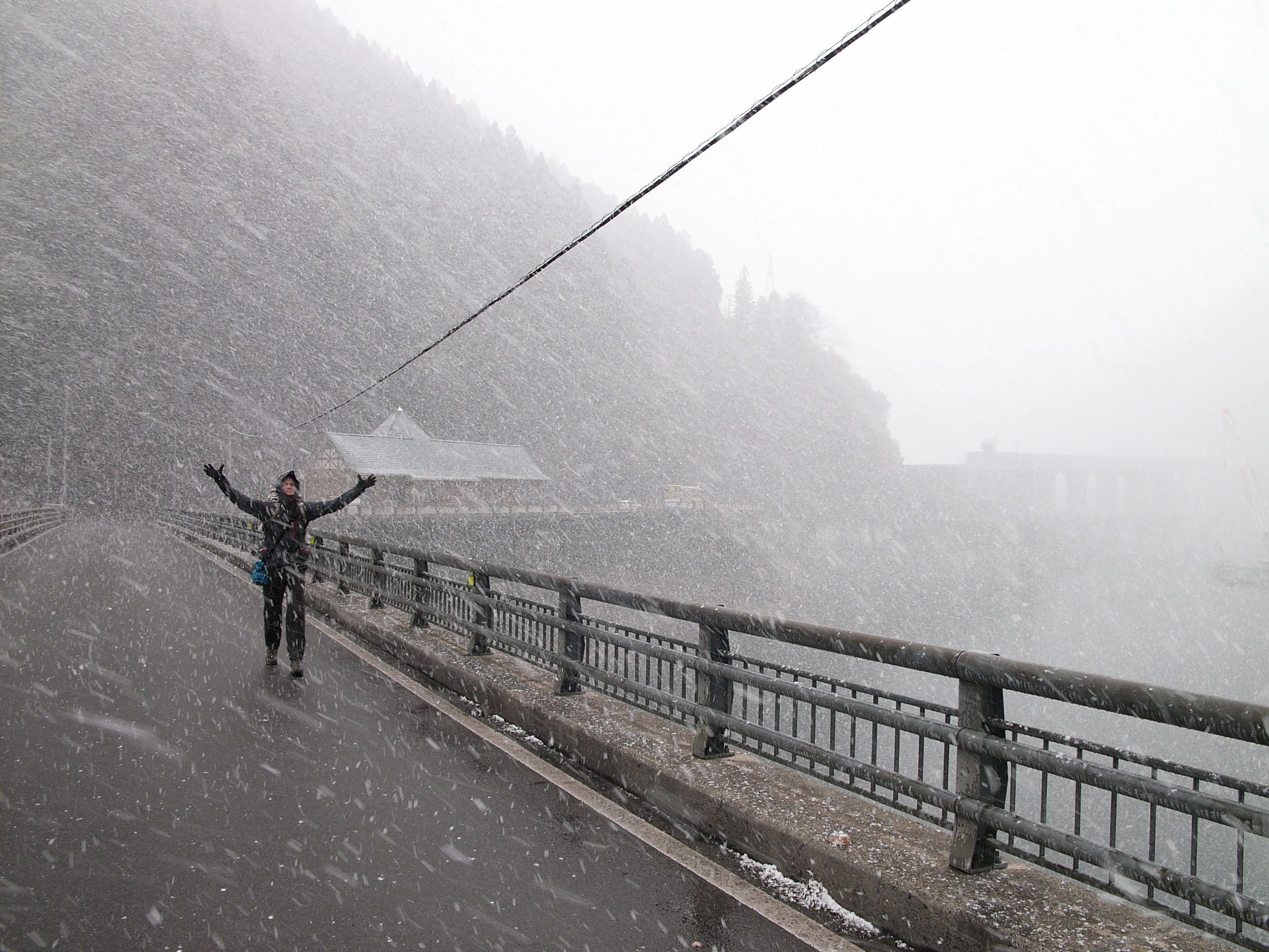 Another man, Gyula Simonyi, walks across a bridge in heavy snowfall, holding his arms above his head.