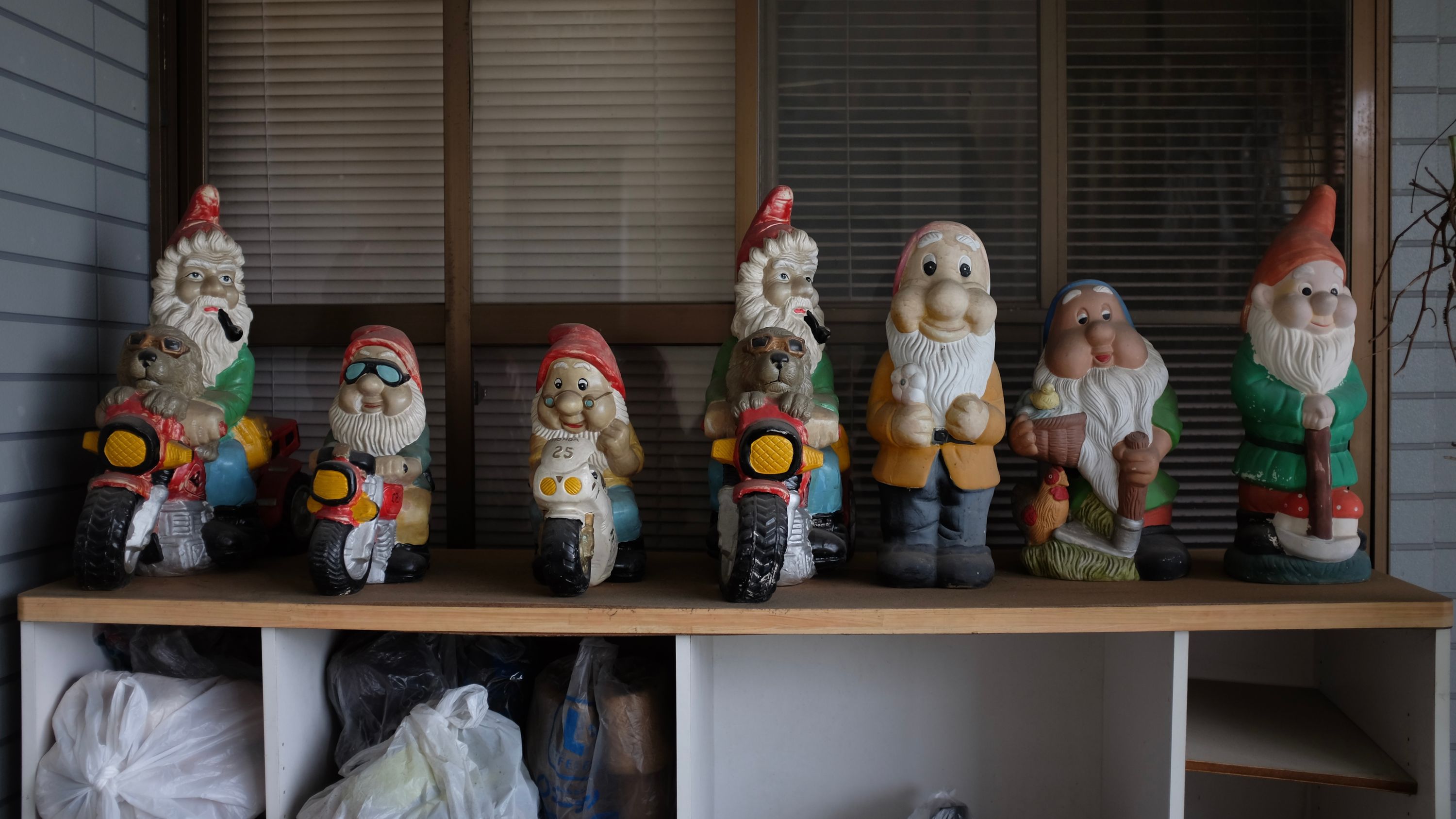 Seven dwarves in Santa hats, four of them riding motorcycles, on a shelf.