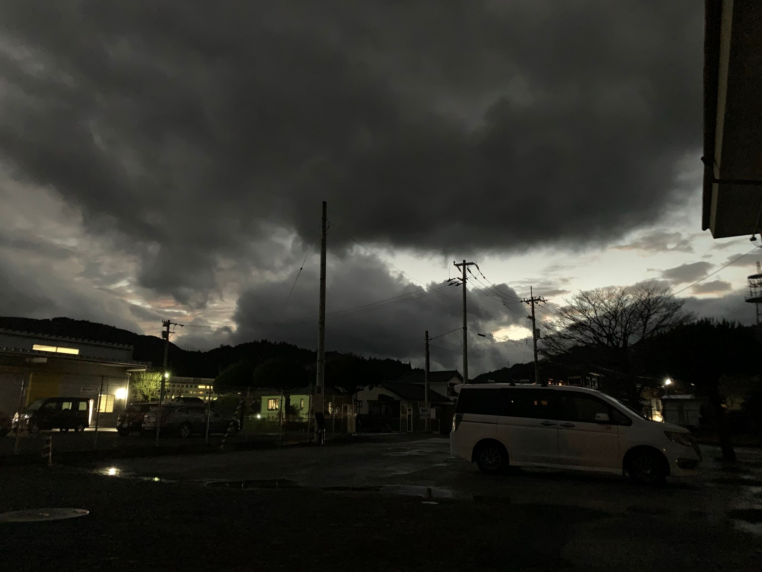 Very dark, almost black clouds above a parking lot at dusk.