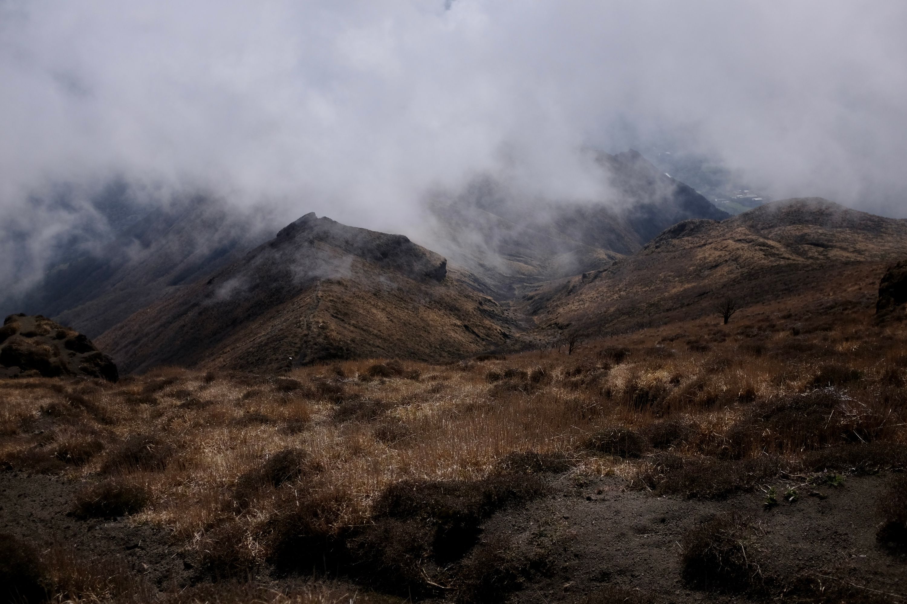 Clouds roll over a yellow-brown grassy landscape on a mountain.