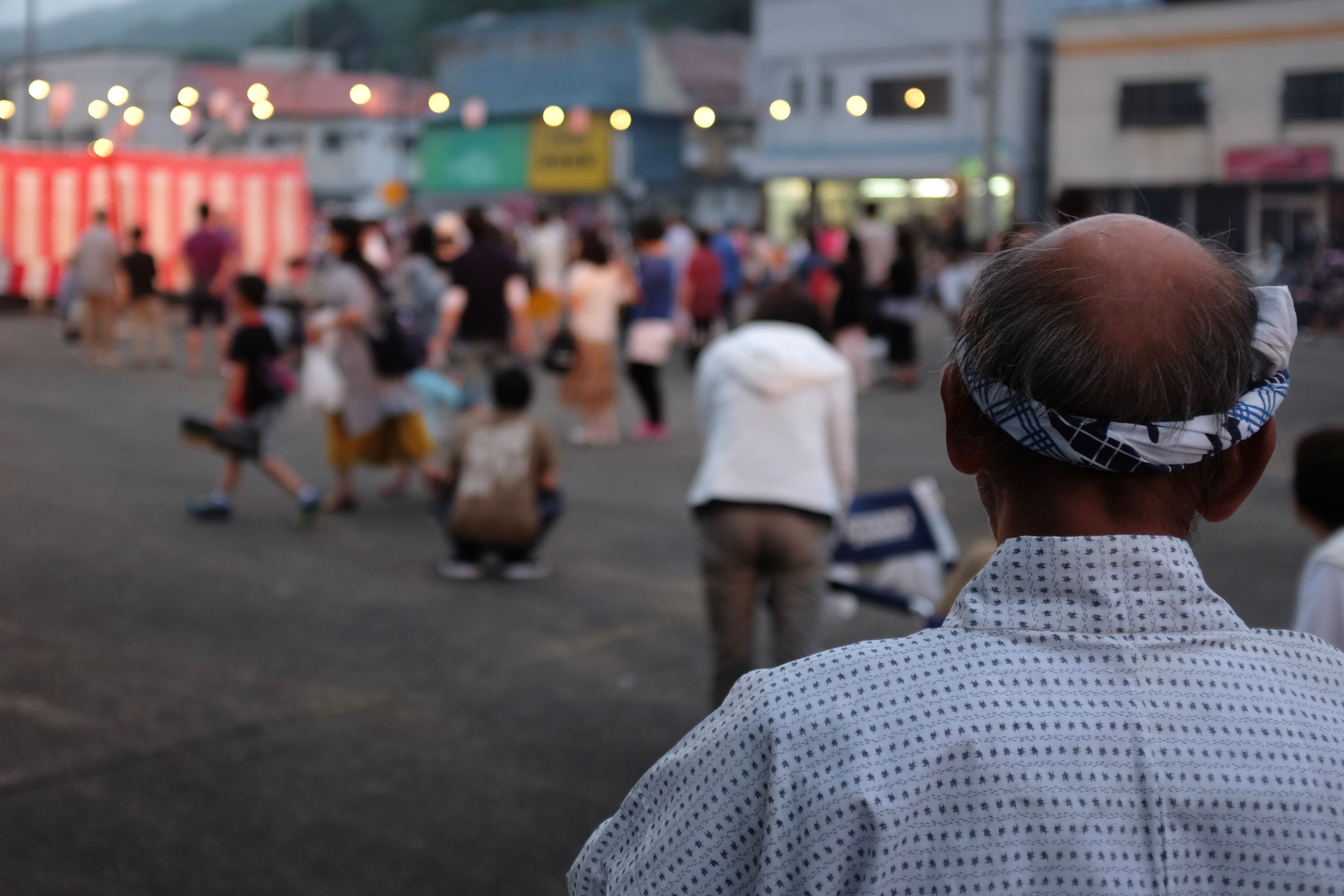 Closeup of the rear of the head of a balding man, wearing a headband and looking out on a group of people.