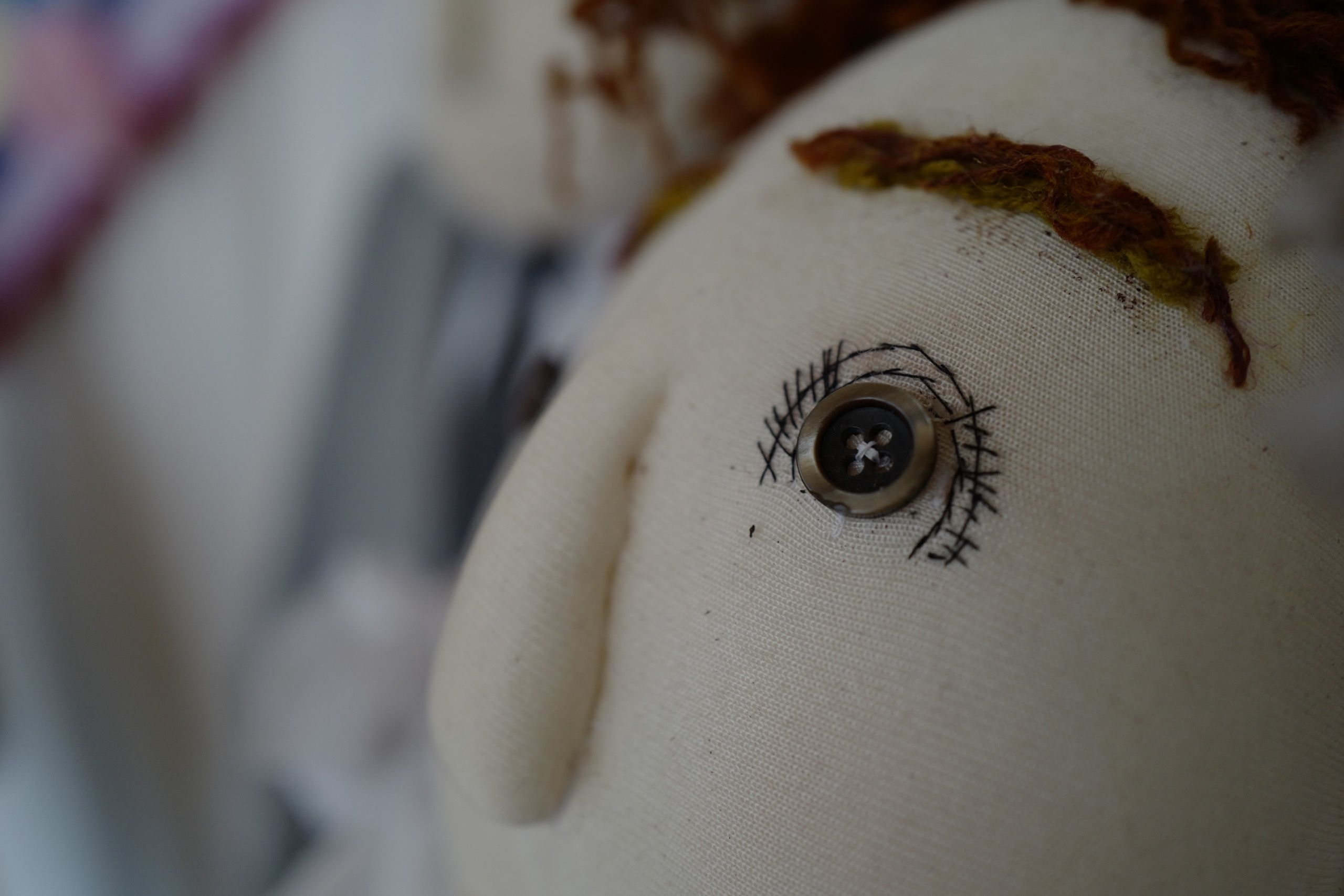 A closeup of the eye, made of a button, of a similar dolls.
