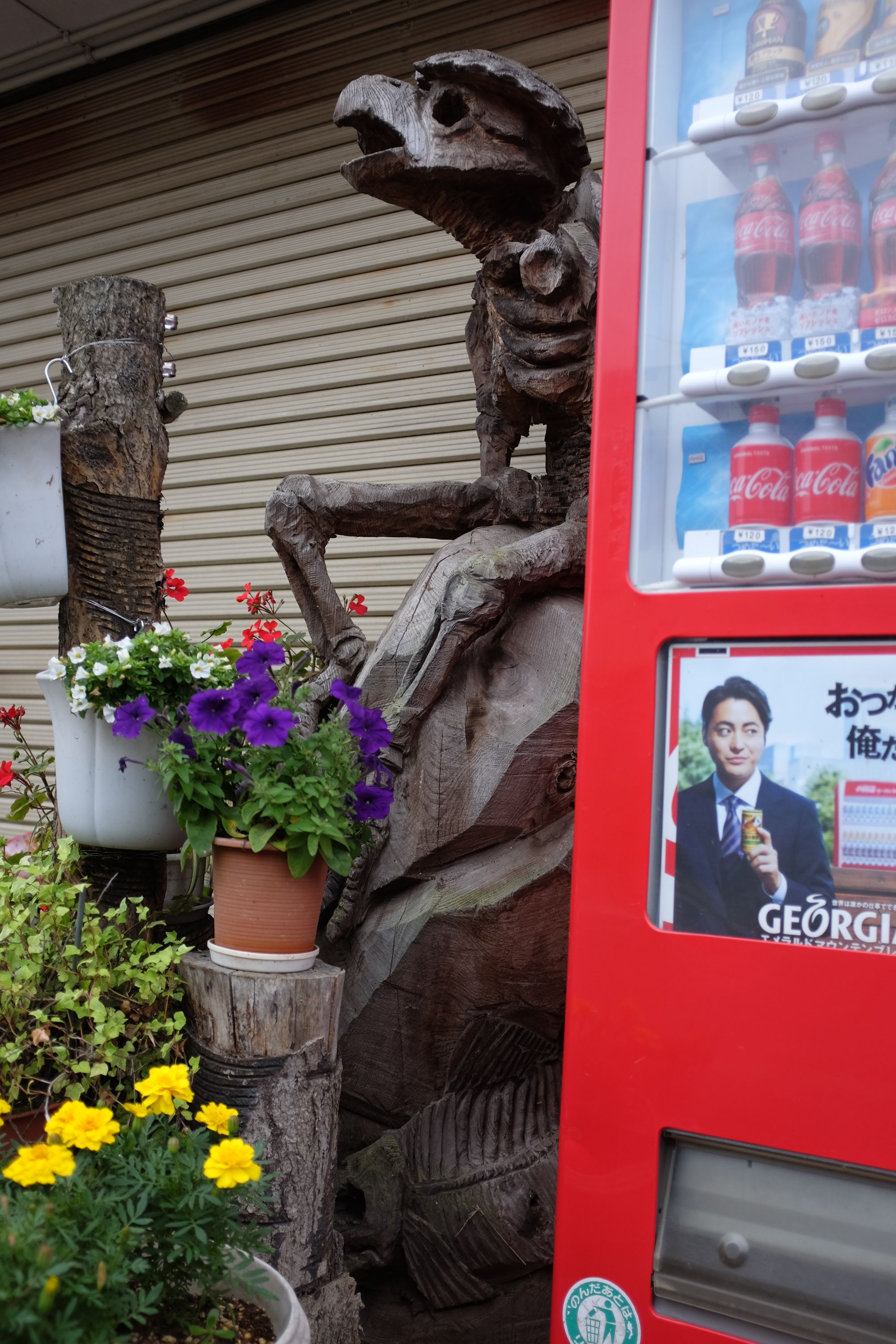 A wooden statue of a one-armed man-turtle next to a vending machine.