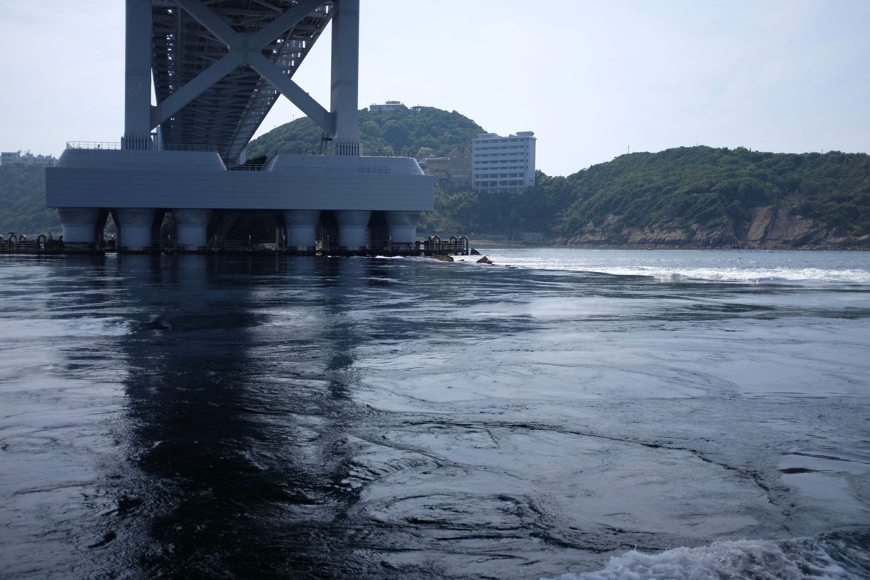 The churning water of the Naruto Whirlpools as seen from a small boat right under the Great Naruto Bridge.