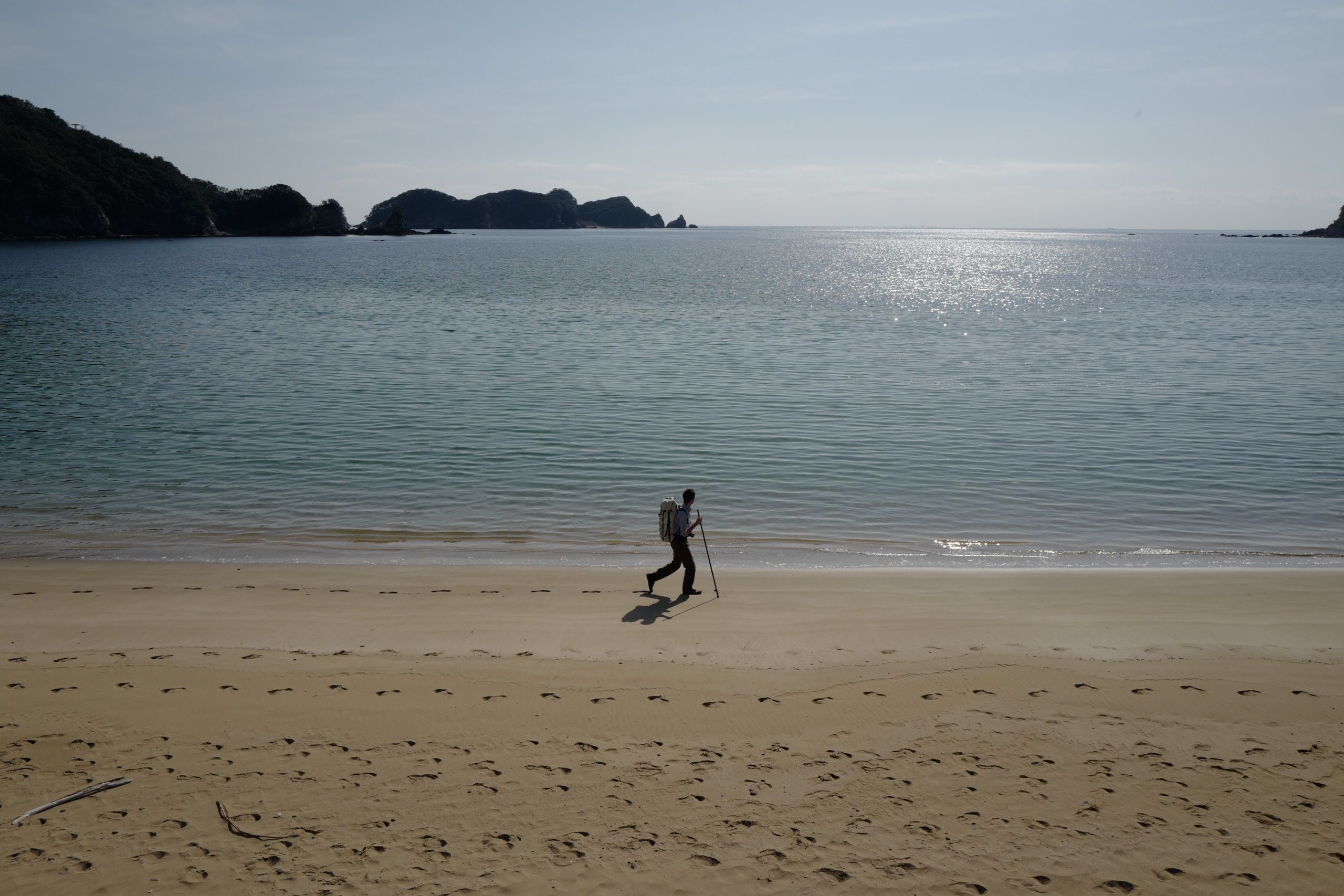 Panorama of a sandy beach with a man, the author, walking along the sea, carrying a rucksack and a walking stick.