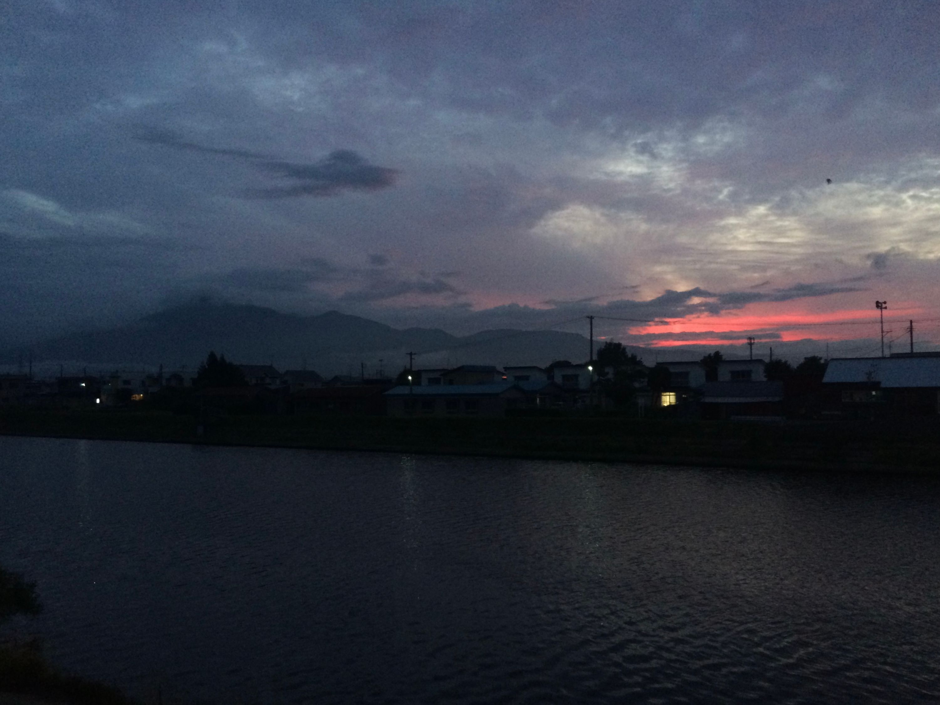 A large mountain, Mount Osore, rises above a small town by the water, Mutsu, in the evening light.