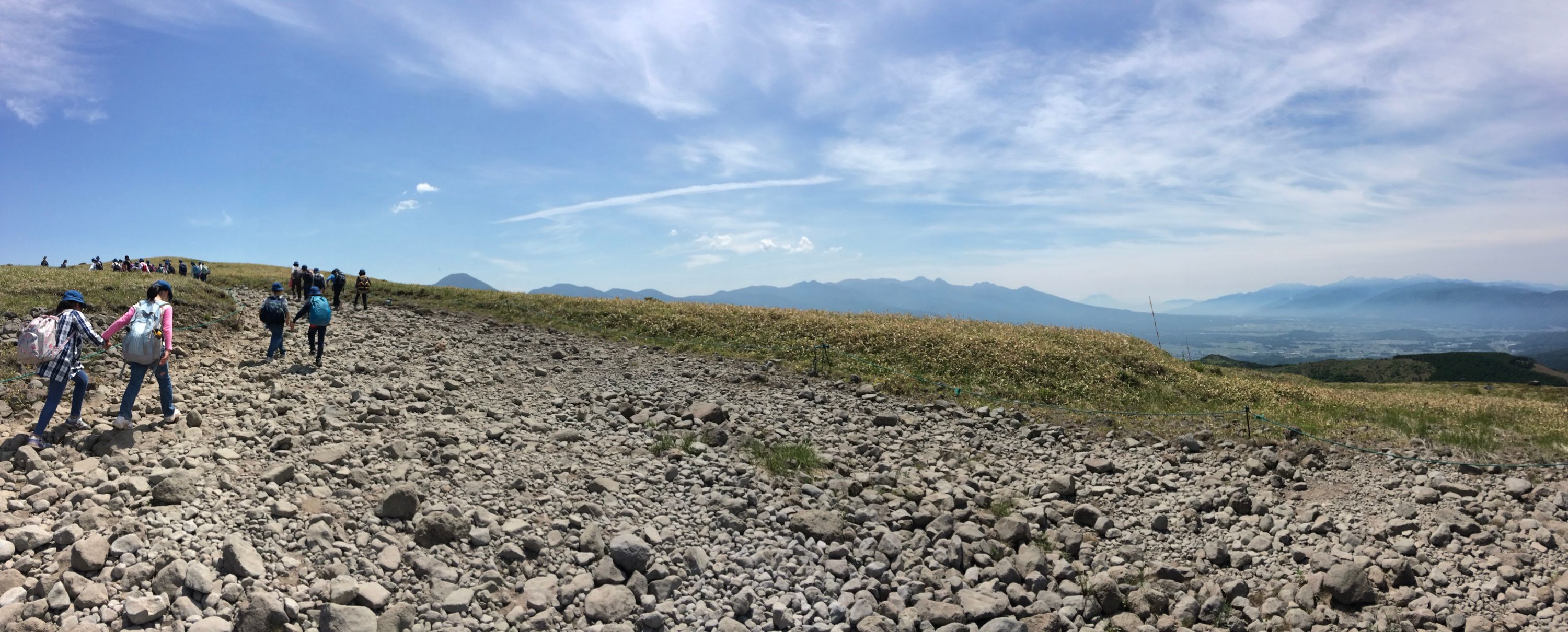 Children climb a trail on a plateau with mountains on the horizon.