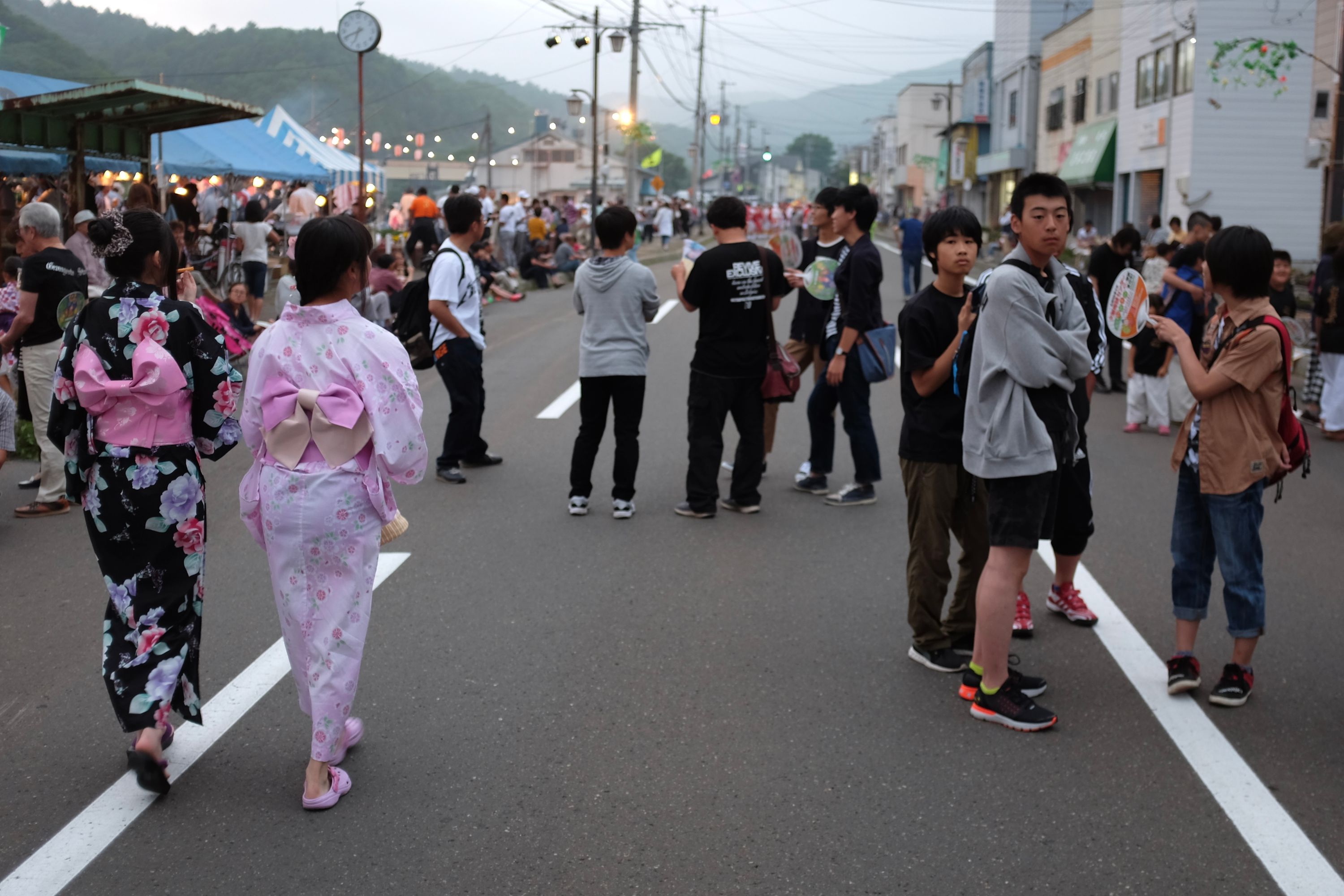 Two young girls in festive clothes walk by a group of boys in regular clothes on a street filled with people.