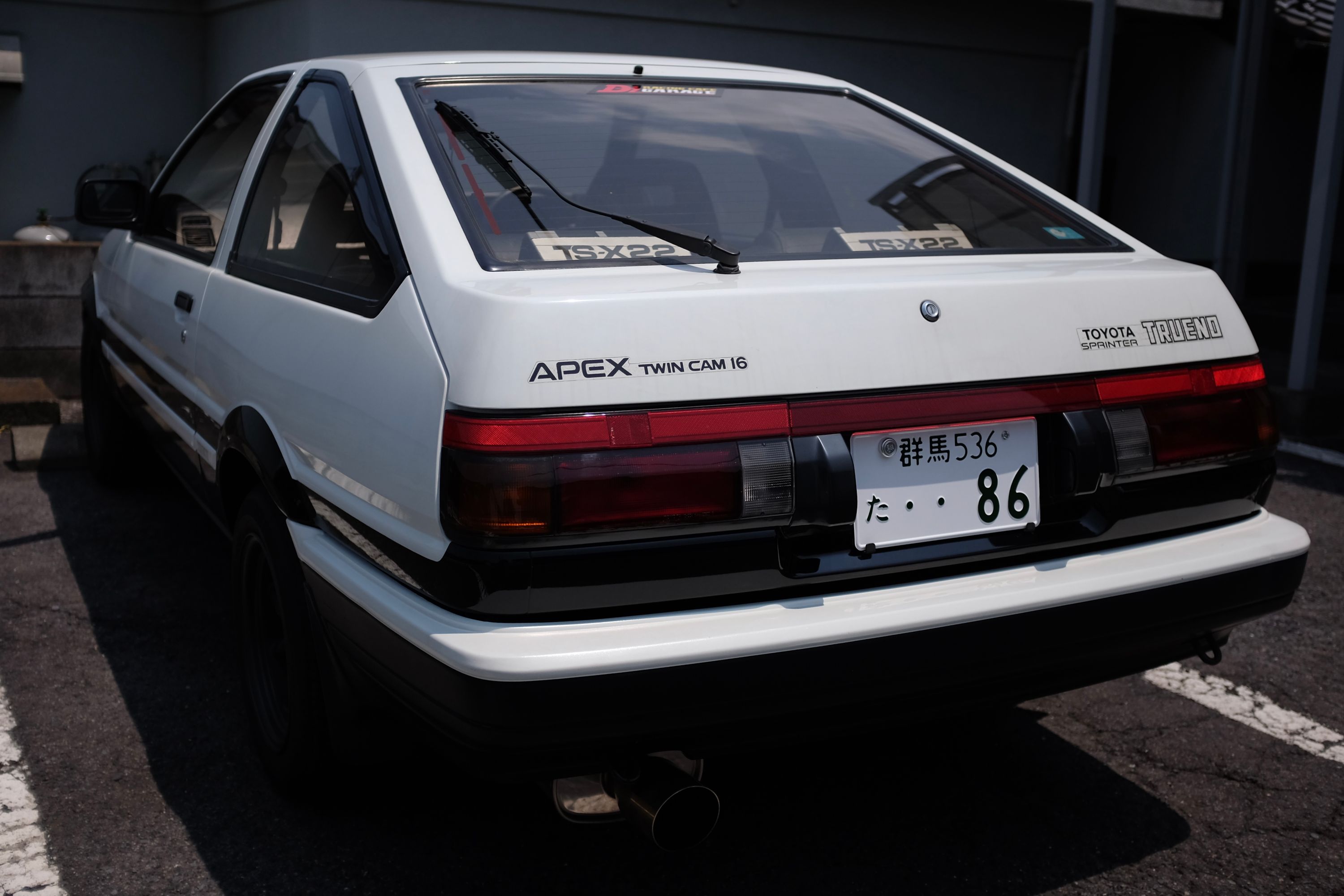 An actual white Toyota AE86 in a parking lot, with the same color scheme as in the anime Initial D.