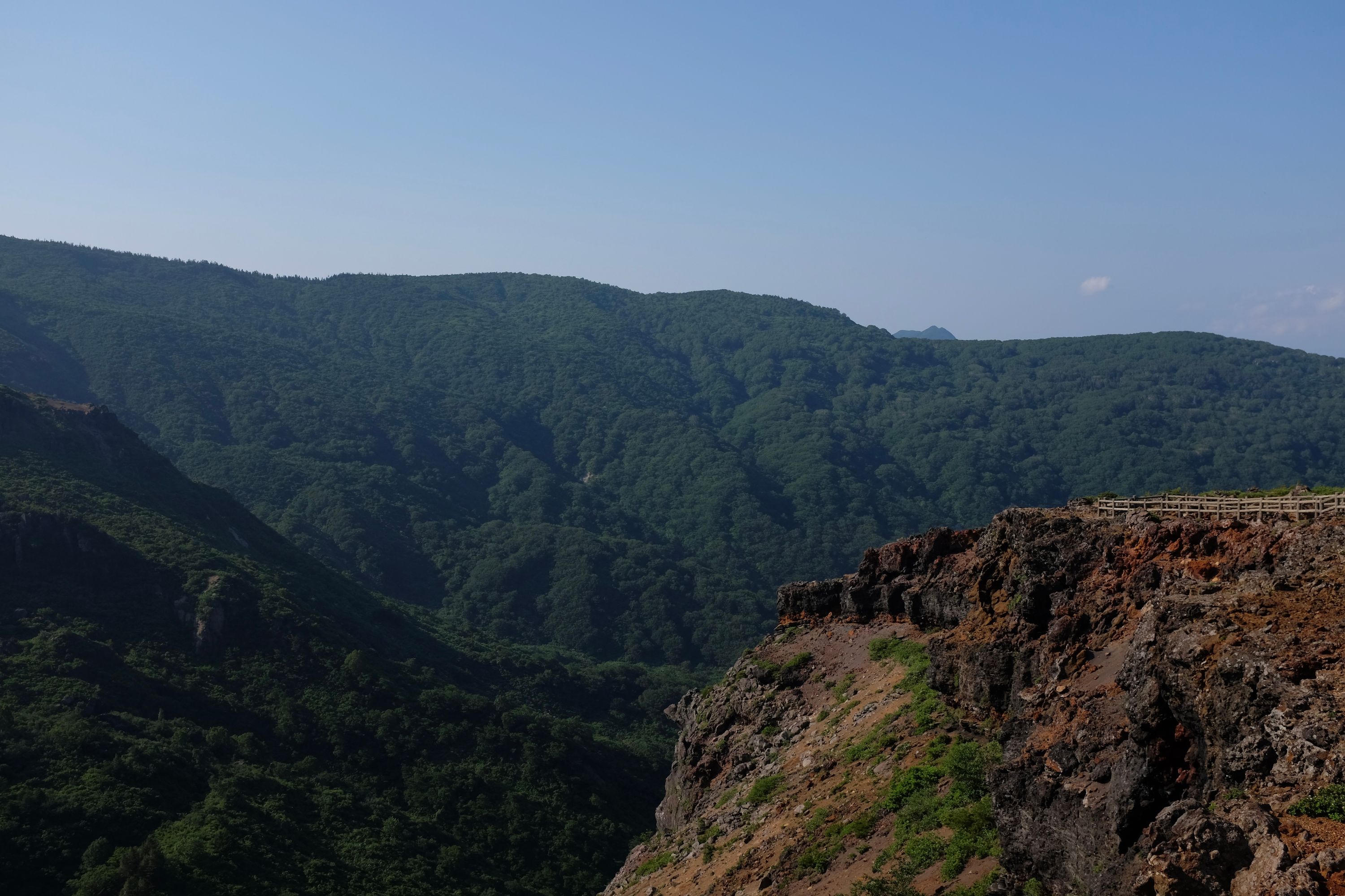 A colorful volcanic cliff, with forested hillsides in the background.