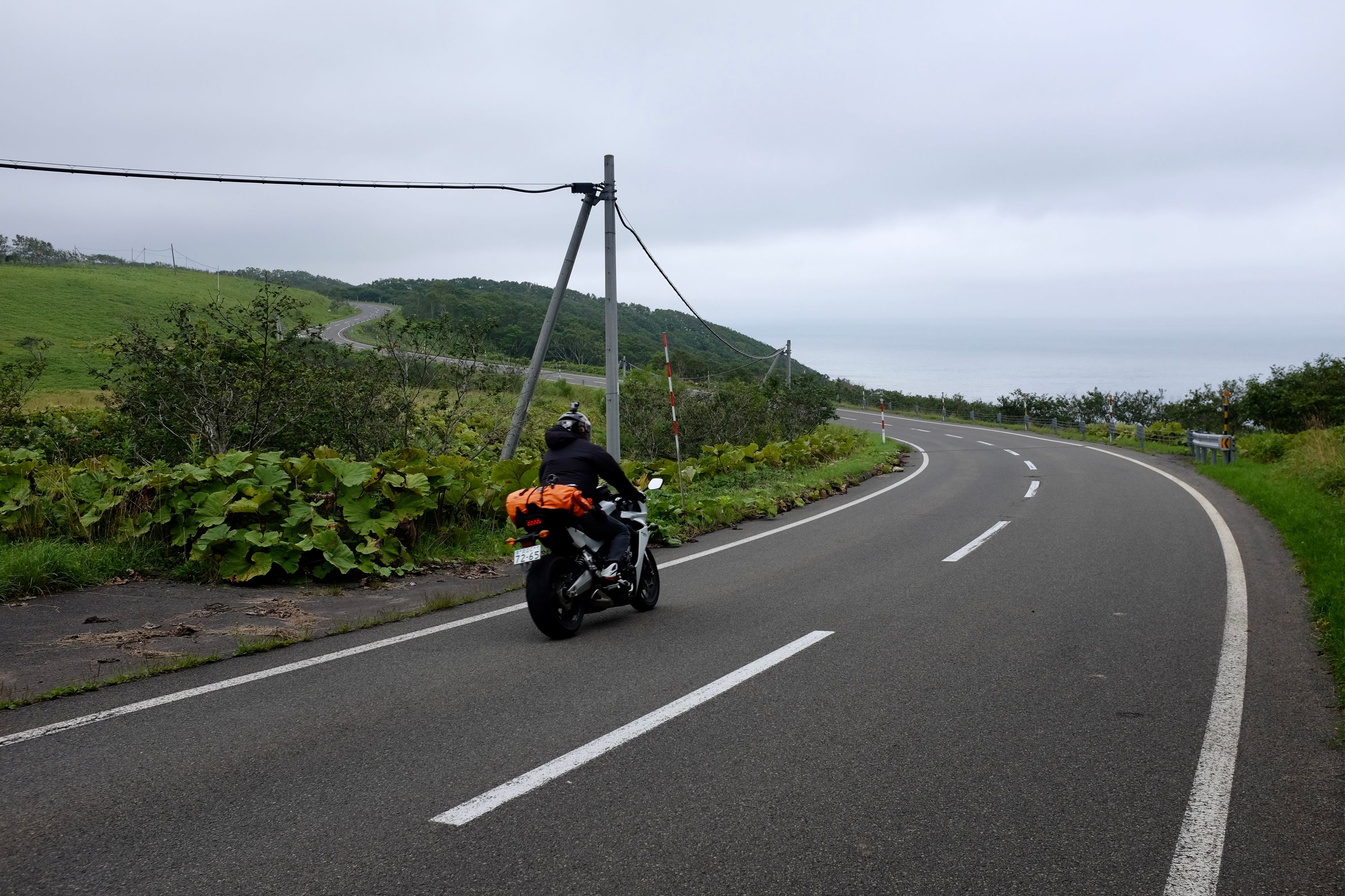 A motorcycle rounds a bend on a coastal road.