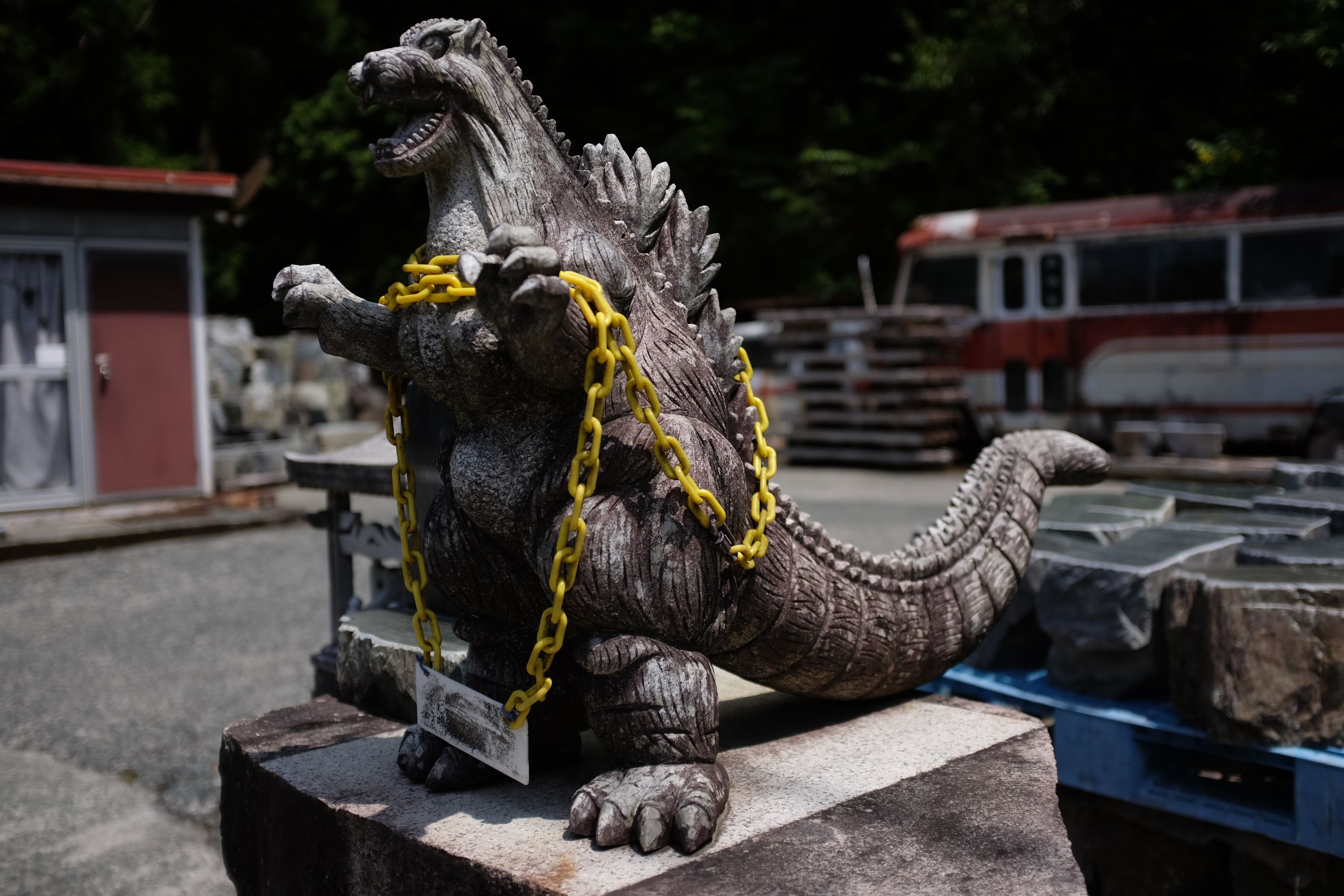 A stone figure of Godzilla bound with a yellow chain at a stoneworker’s shop.