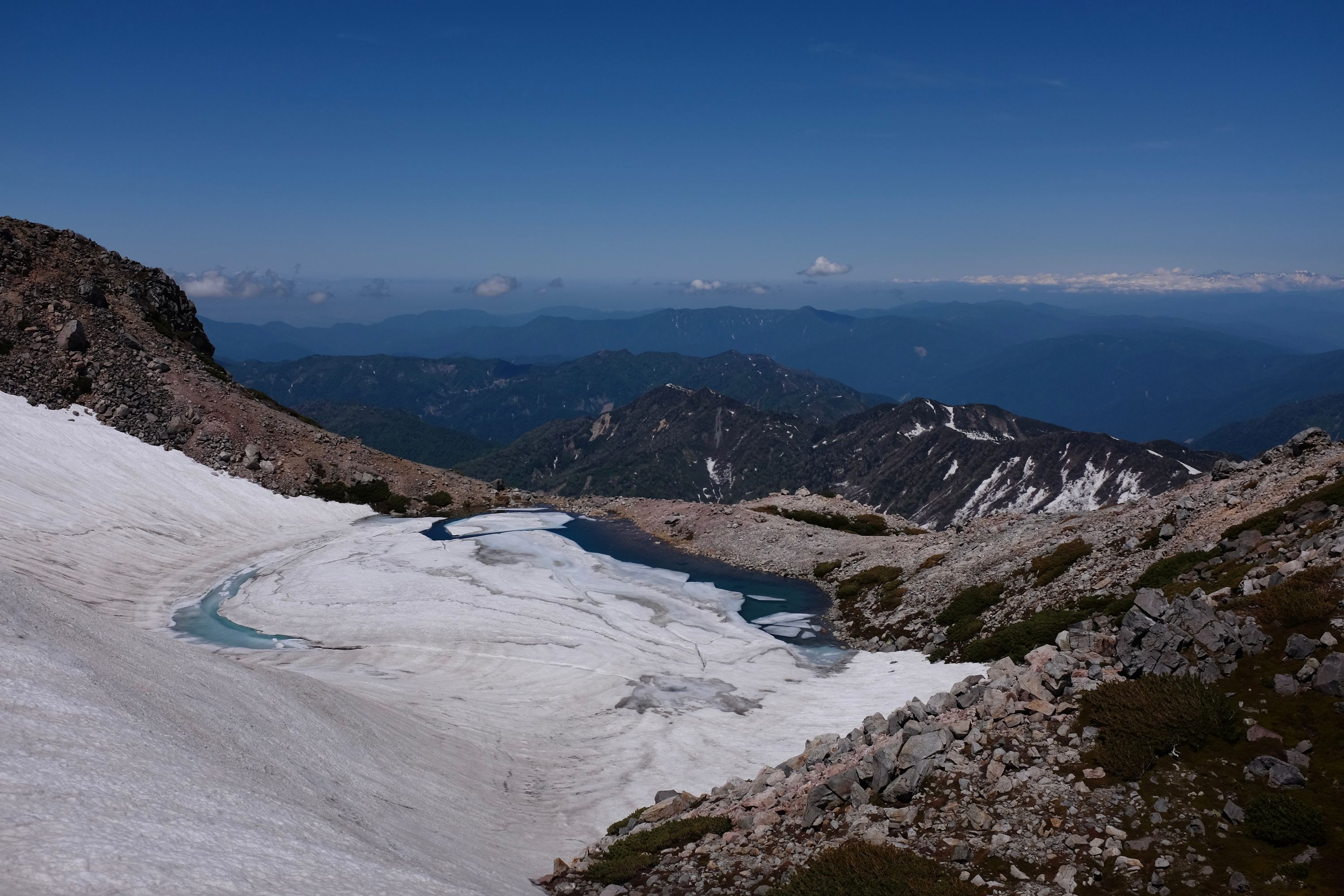 Looking out over a crater lake, mostly frozen over, across the lower ridges of Hakusan, towards the Hida Mountains.